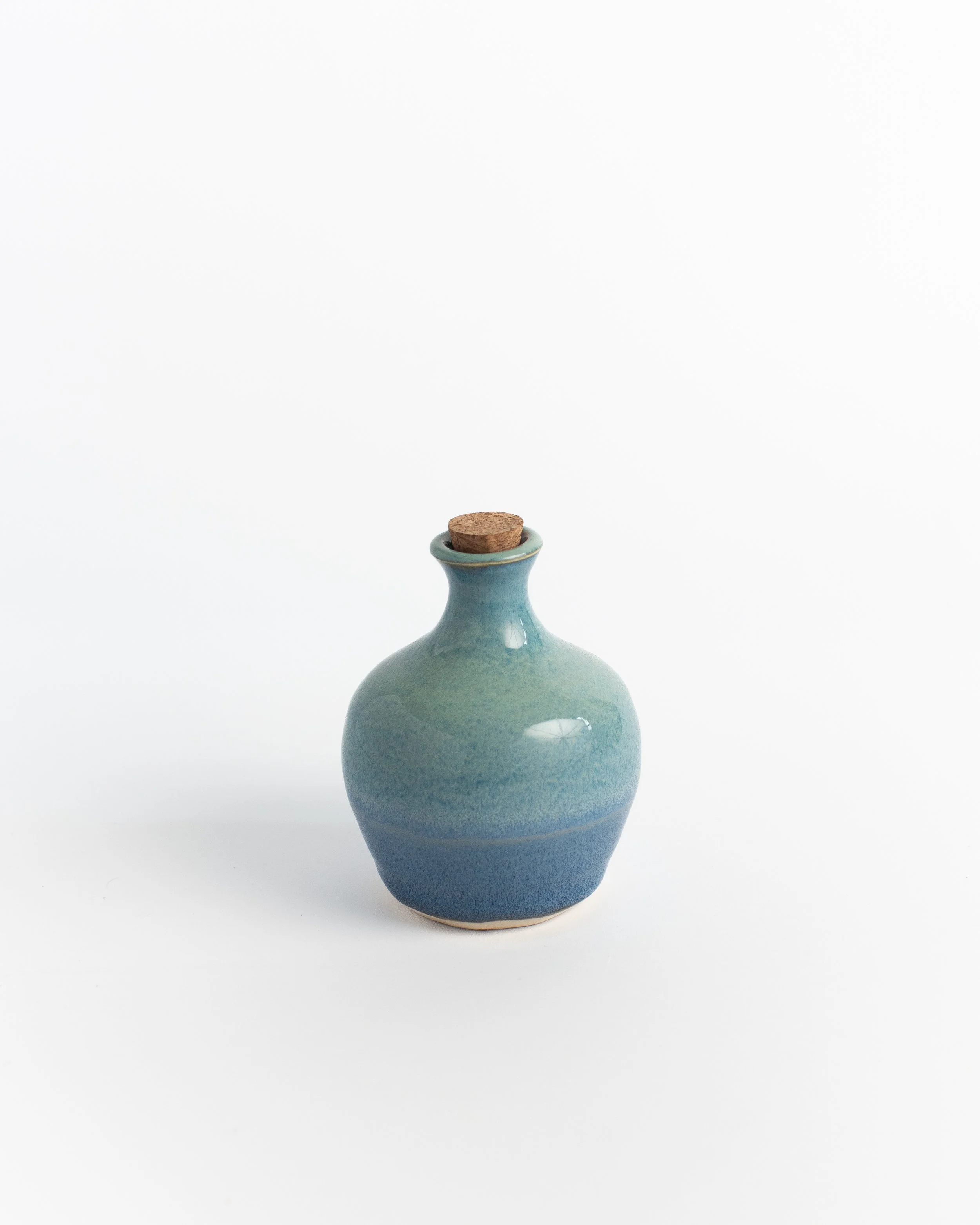 Rounded corked ceramic bottle in soft blue shading from sky to sea, with a cork stopper.