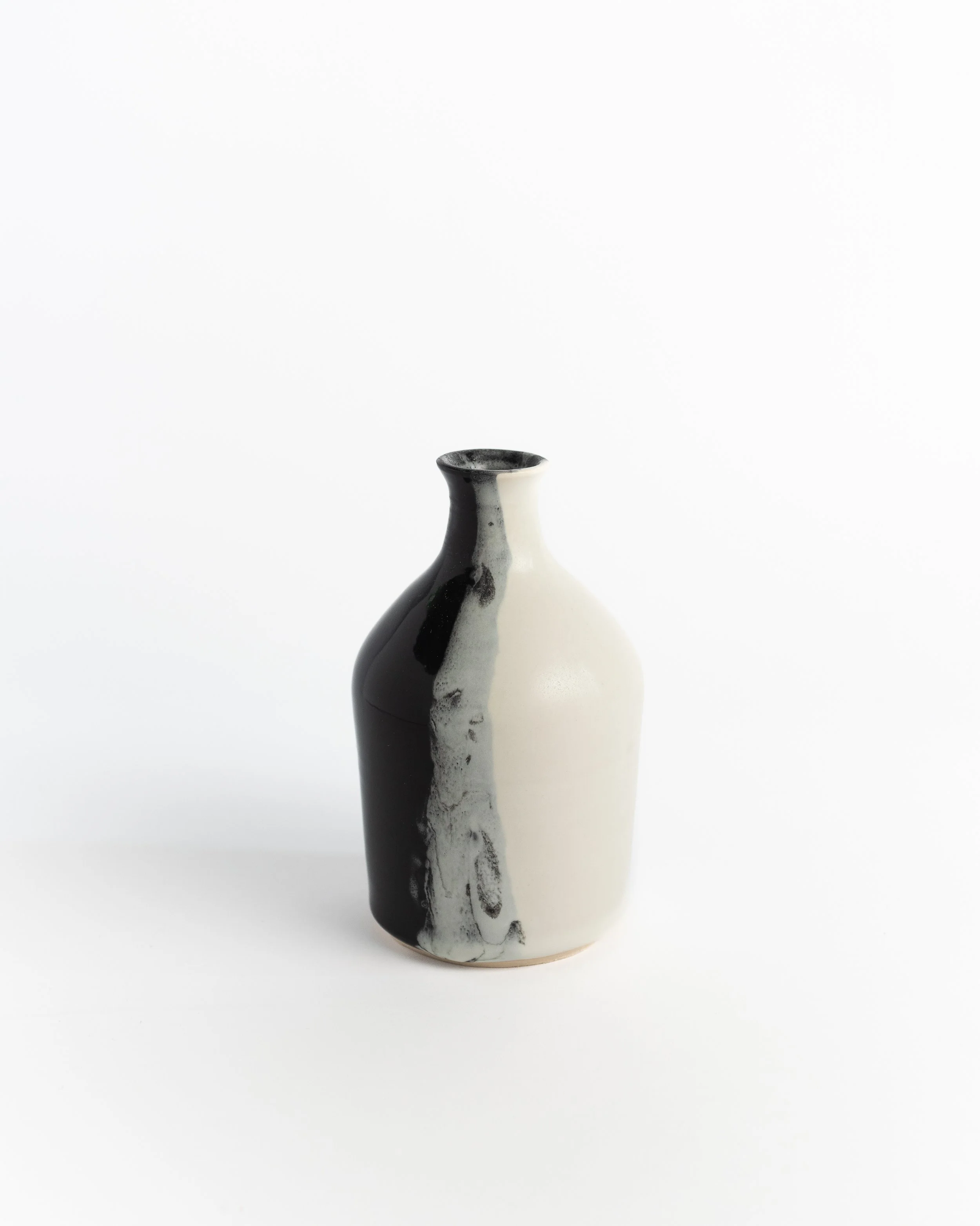 Tall ceramic bottle vase split between cream white and glossy black with an inky seam down the middle.