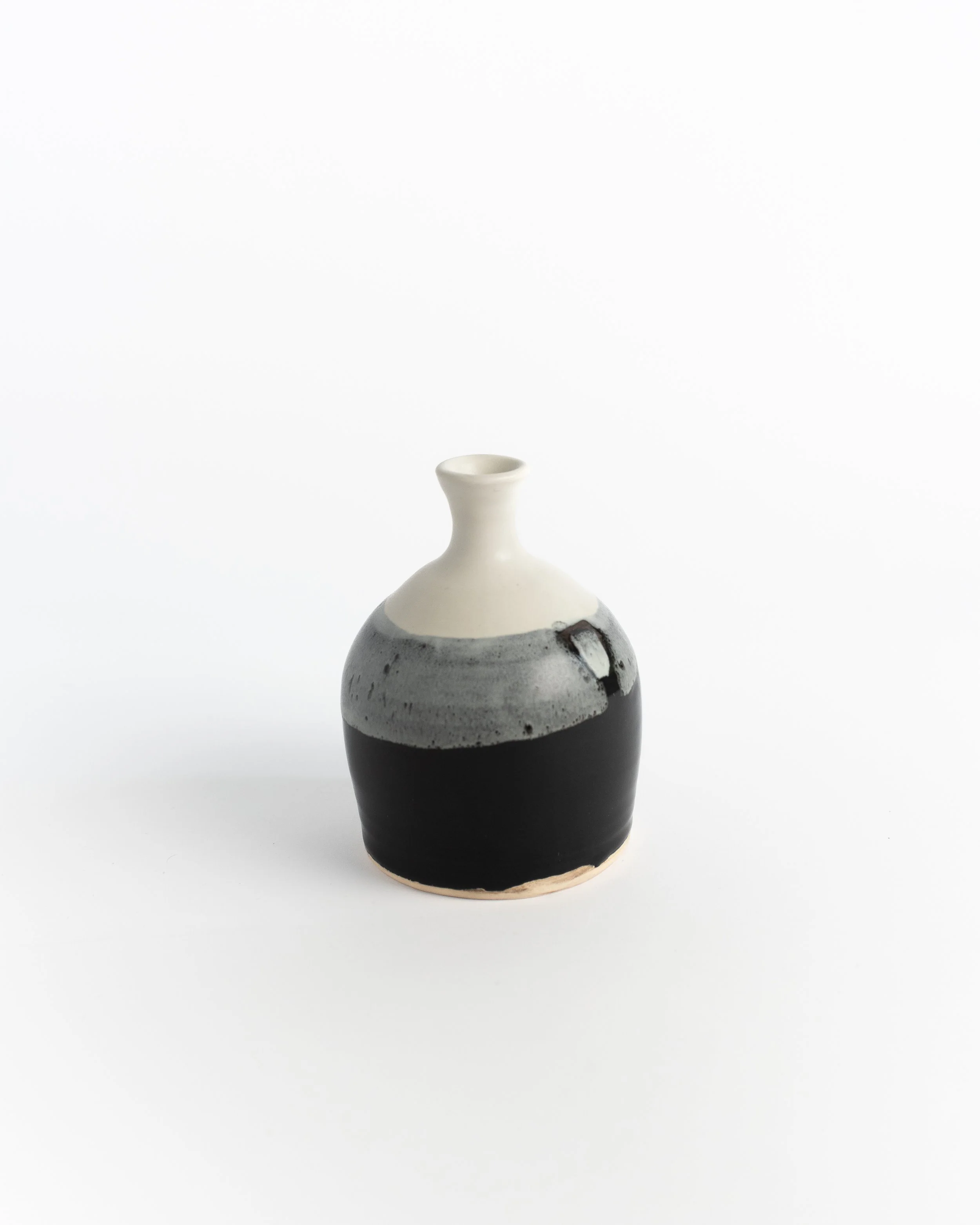 Small ceramic bud vase dipped in glossy black beneath a smoky grey and white shoulder.