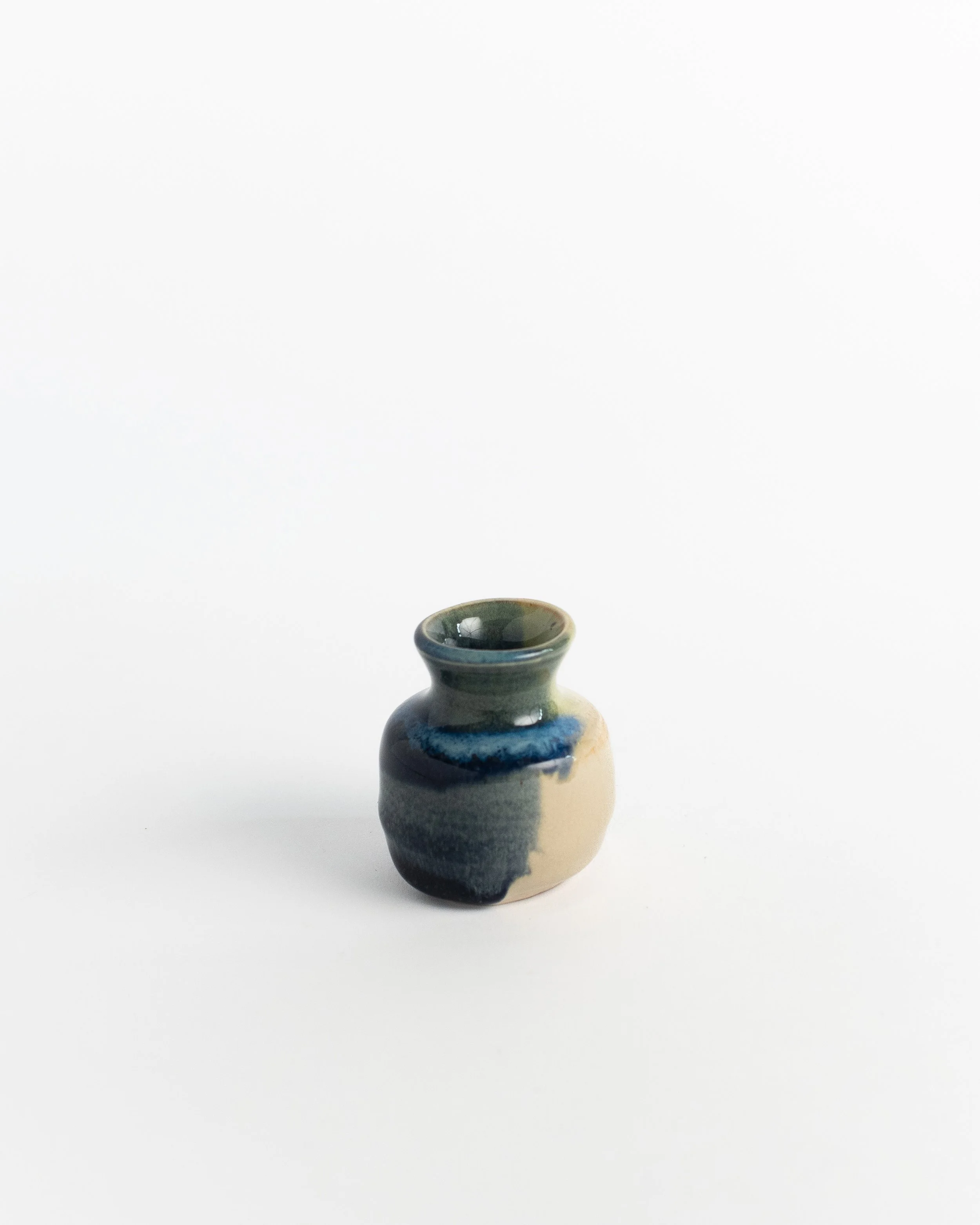 Petite ceramic bud vase in cream washed with deep blue and a green-grey rim.