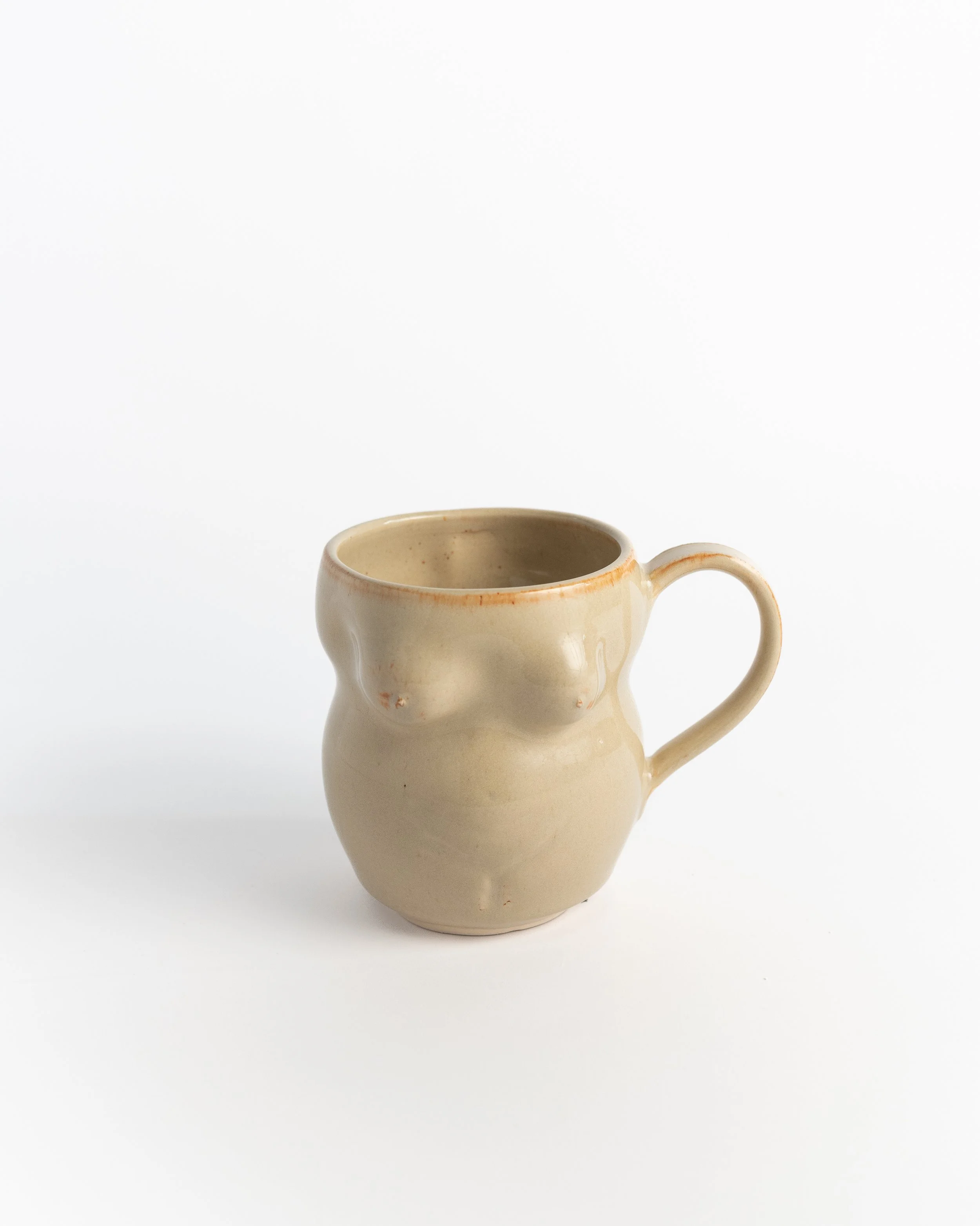 Sculptural ceramic mug in warm oatmeal glaze, hand-shaped into a softly curving figure.