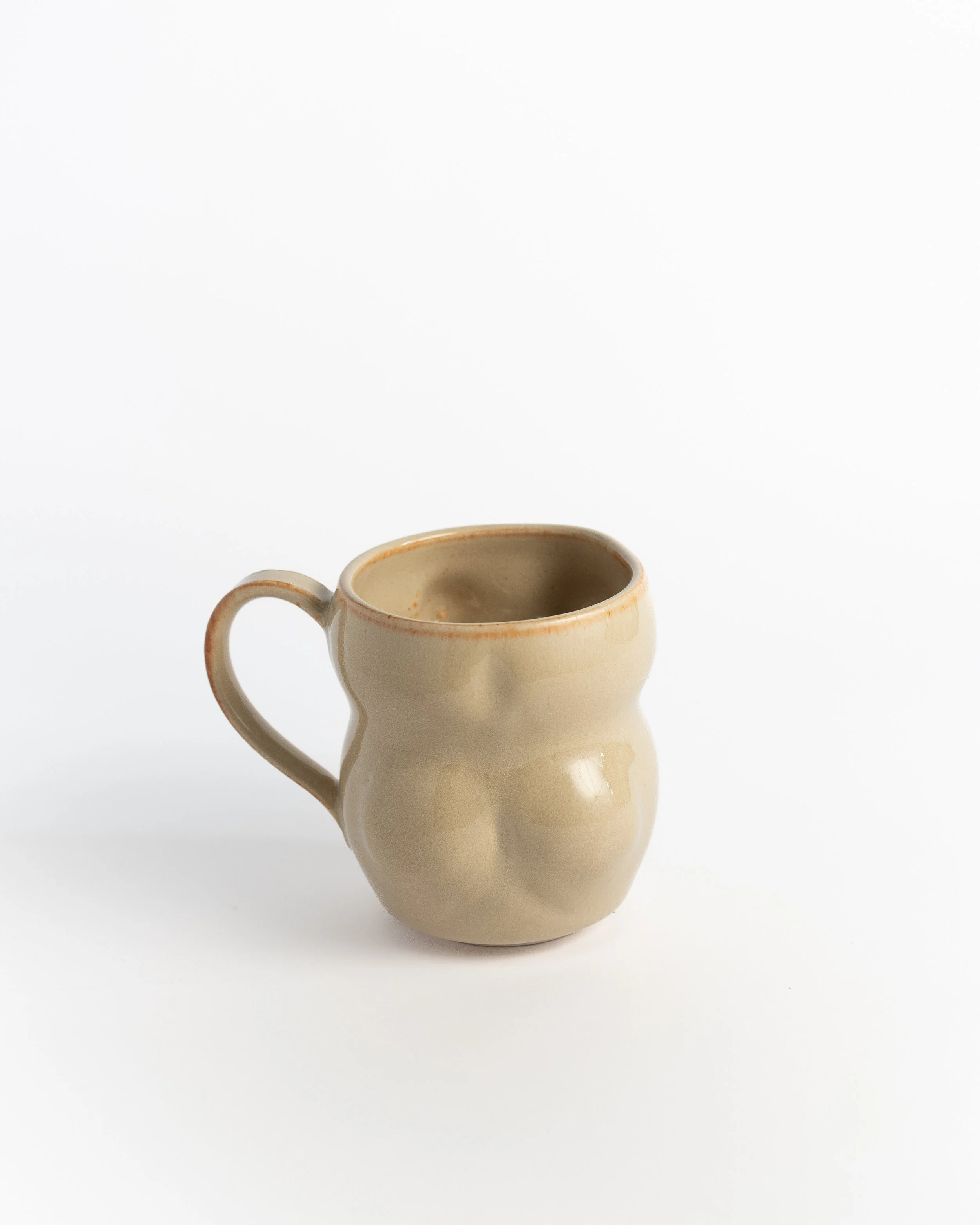 Sculptural oatmeal ceramic mug seen from behind, showing the curved body and looped handle.