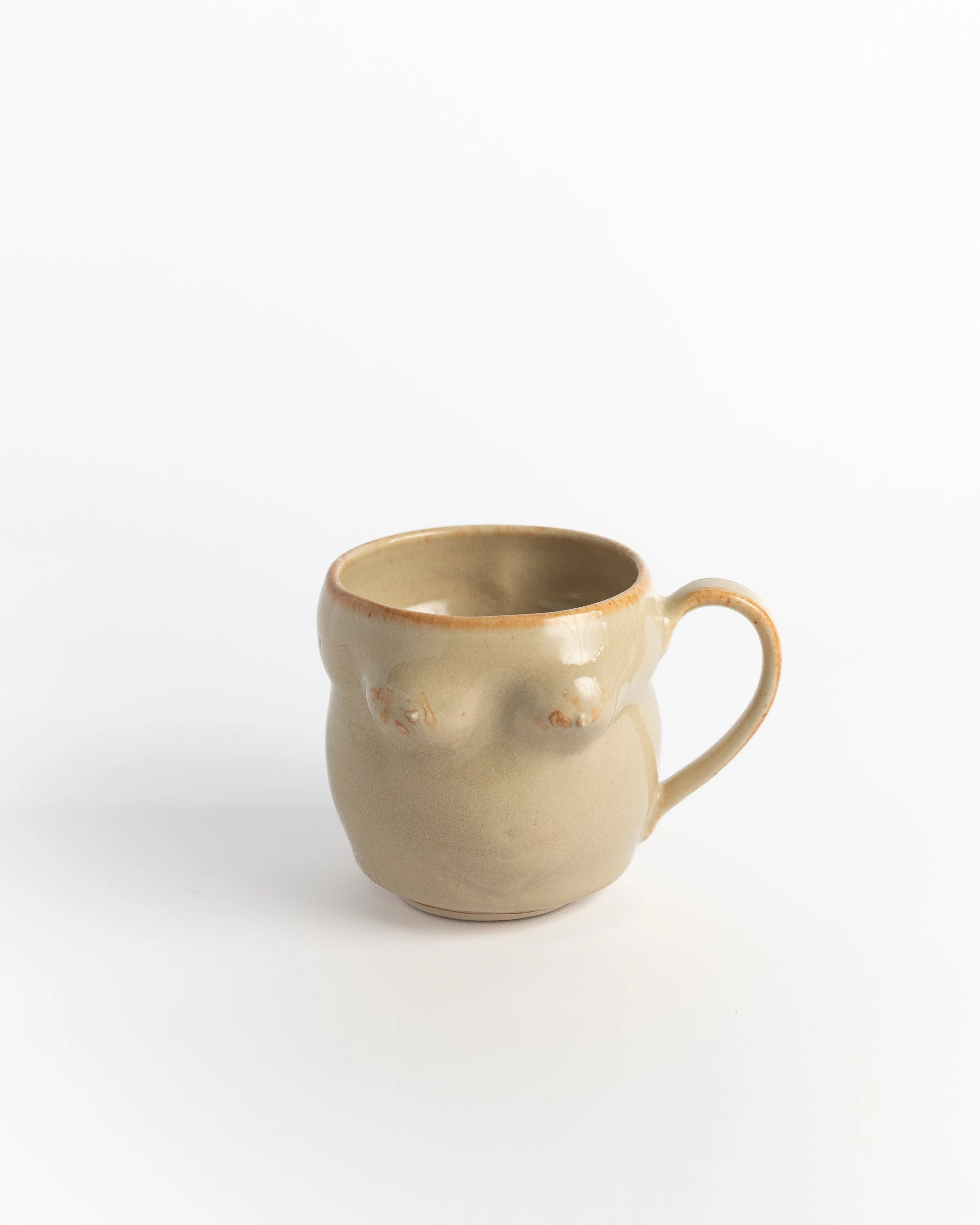 Sculptural ceramic mug in warm oatmeal glaze, hand-shaped into a softly curving figure.