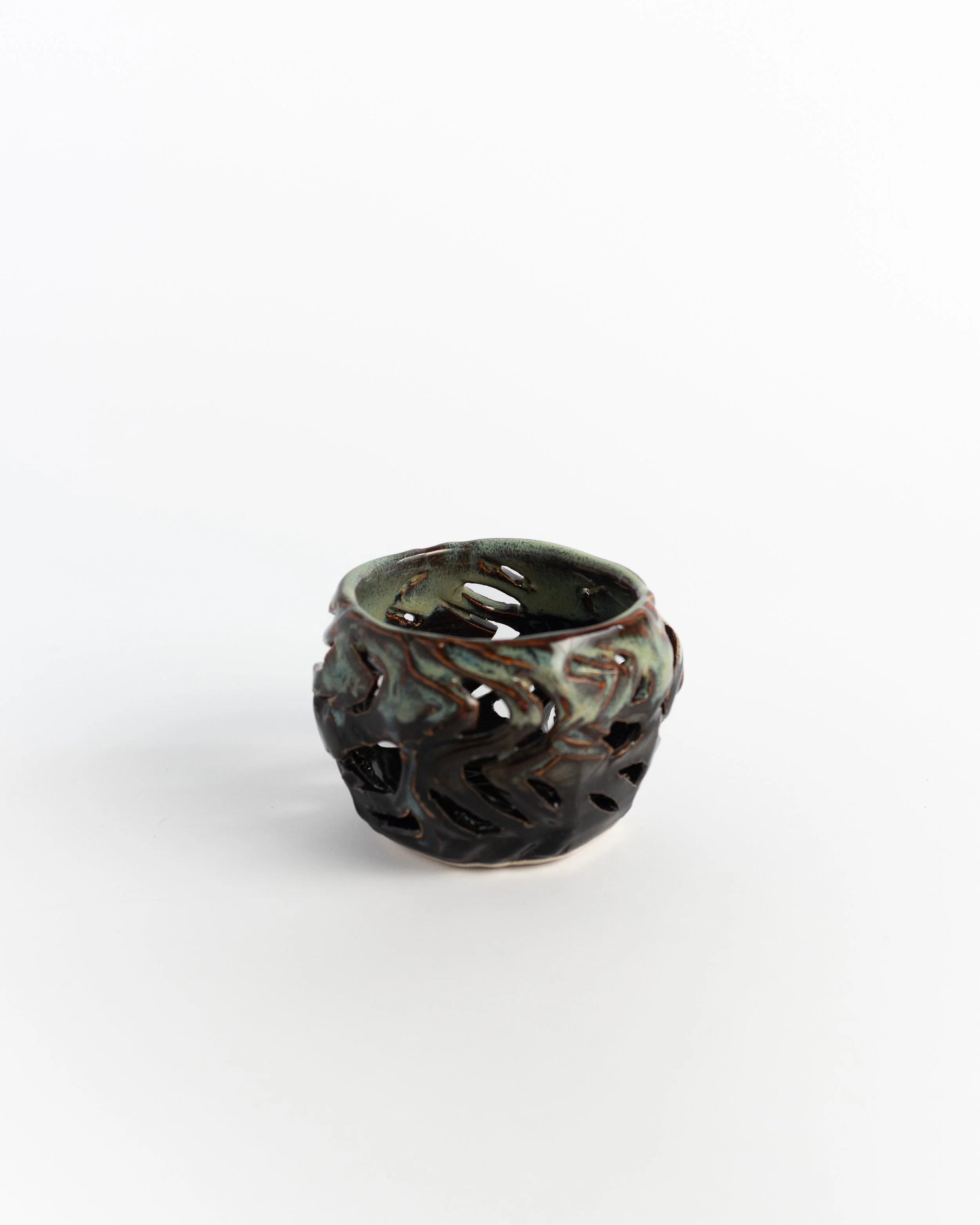 Carved openwork ceramic votive in dark bronze-green with cut walls that scatter candlelight.