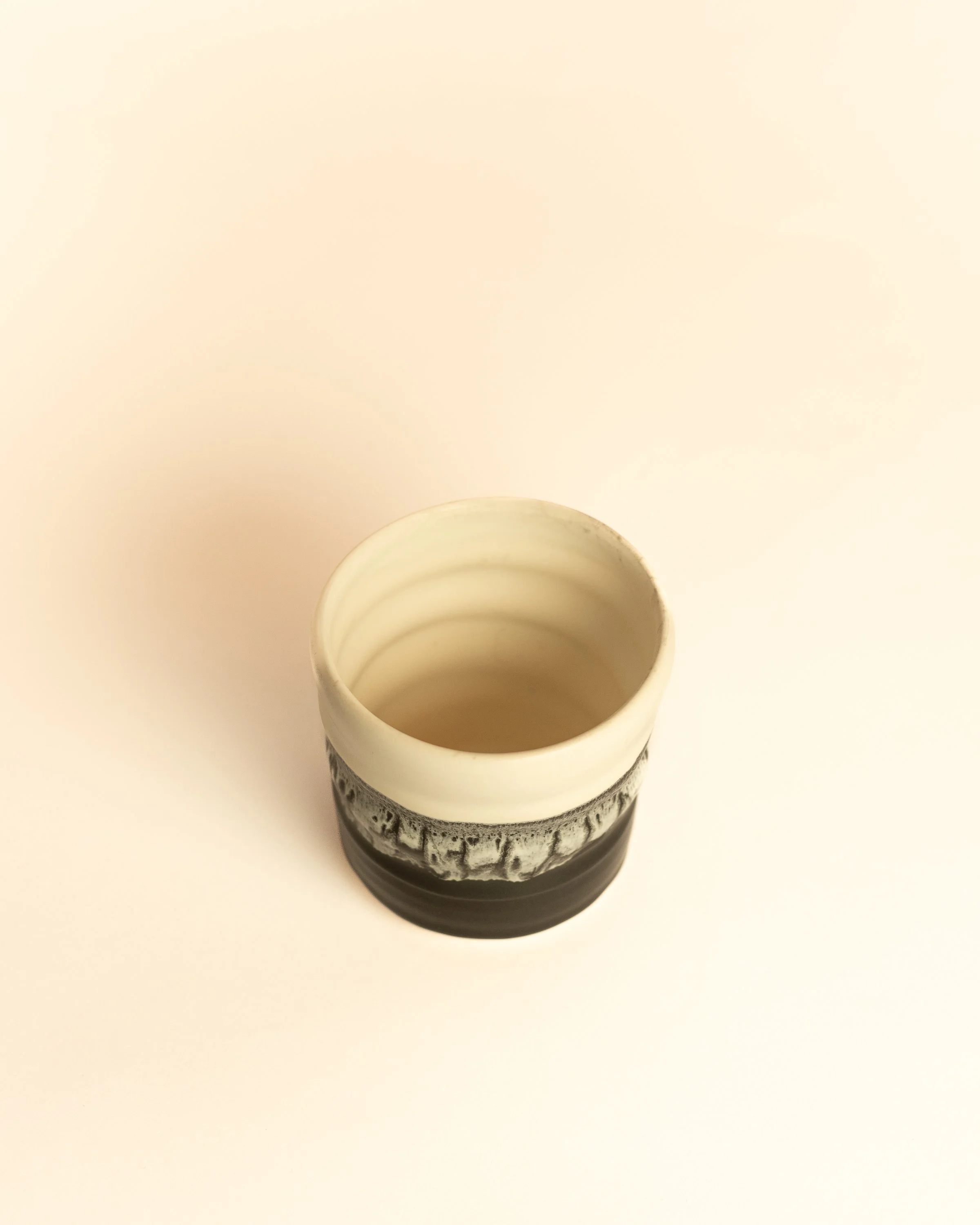 Cream interior of a handleless ceramic cup above a grey crawl band and black base.