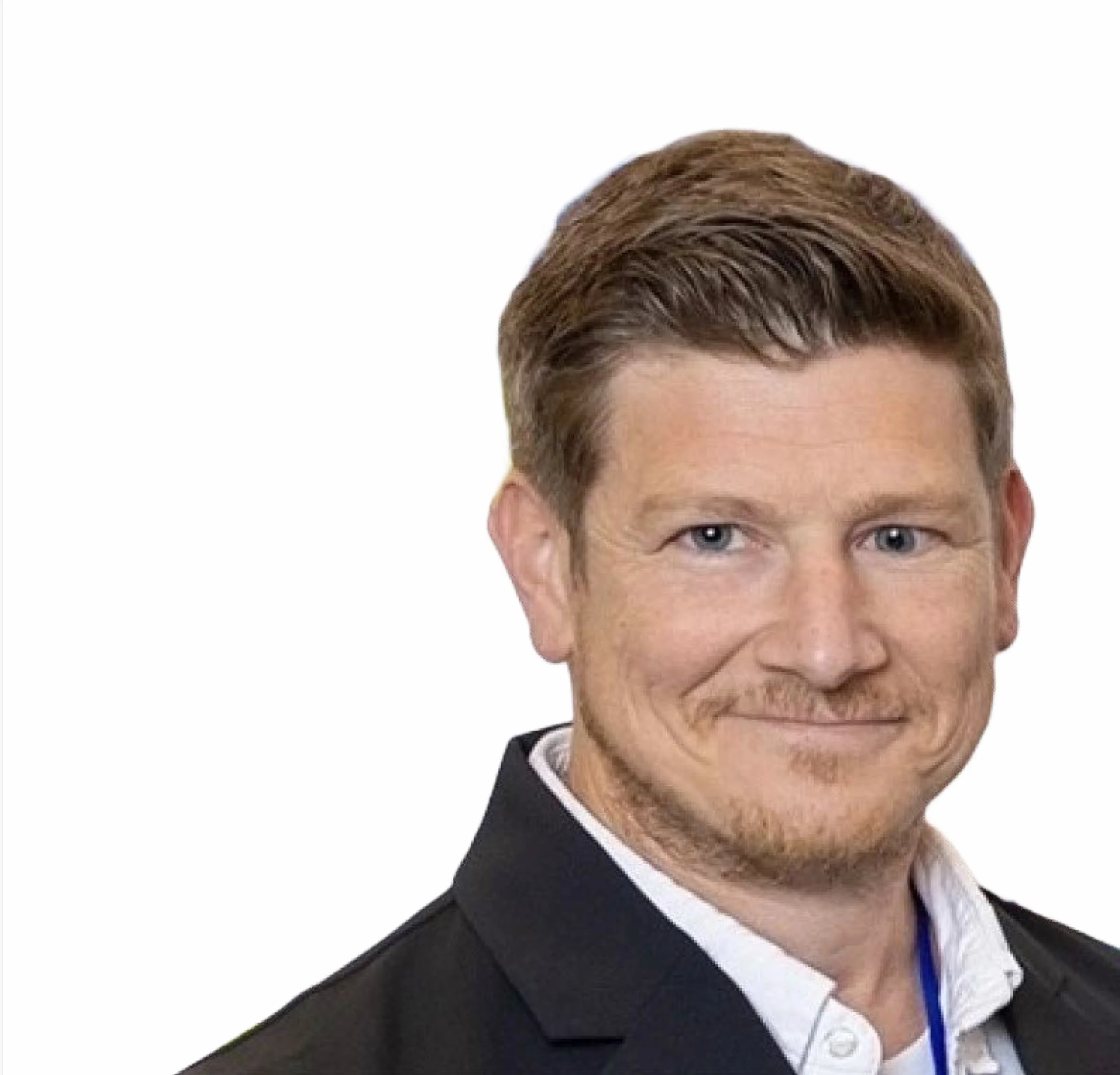Close-up of a man with ginger hair and a short beard, wearing a suit jacket and white collared shirt, smiling against a white background.
