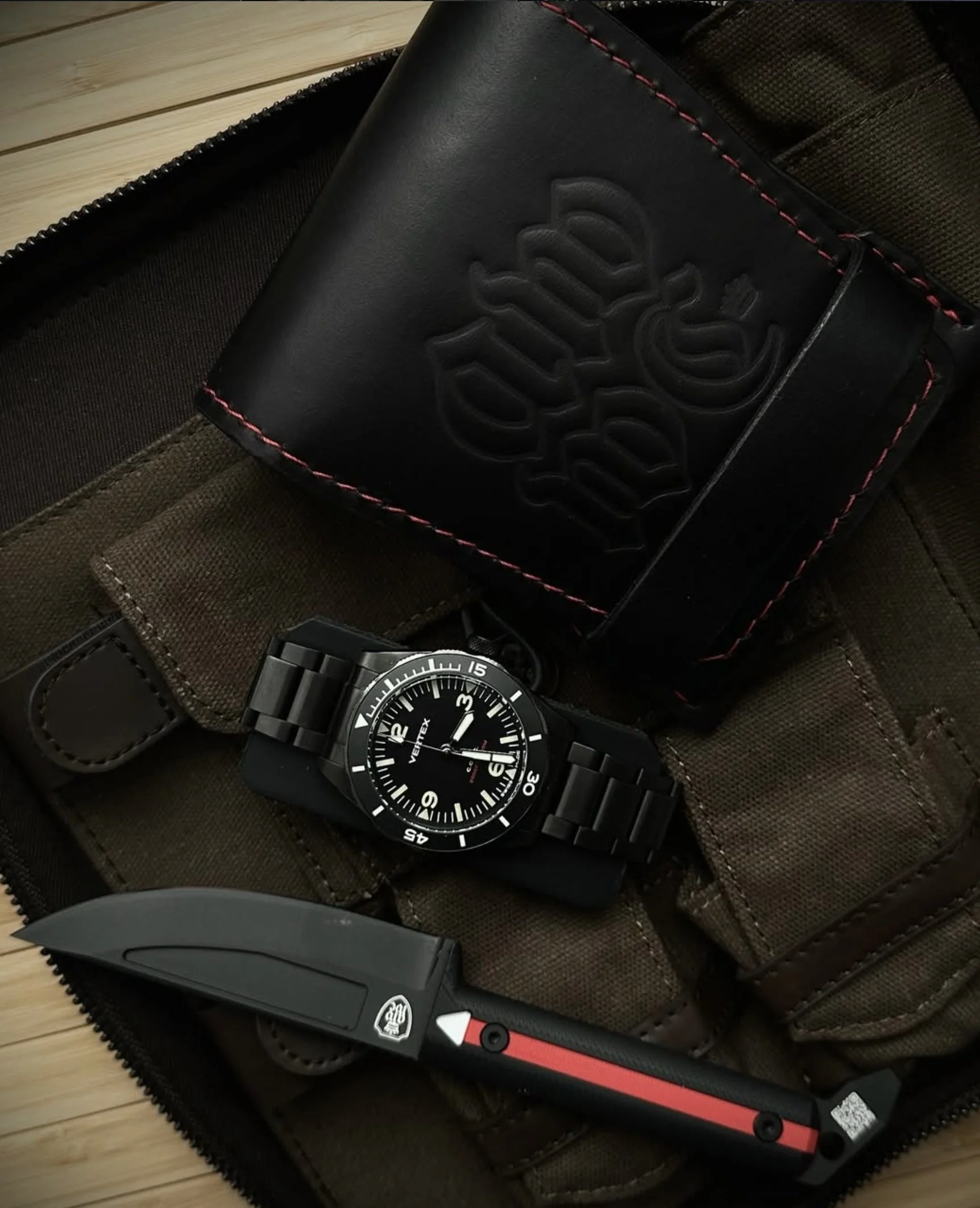 A black wristwatch with a black band, large white numbers, and a black face, placed next to a Swiss Army knife with a red handle and black blade, inside a brown textured case.