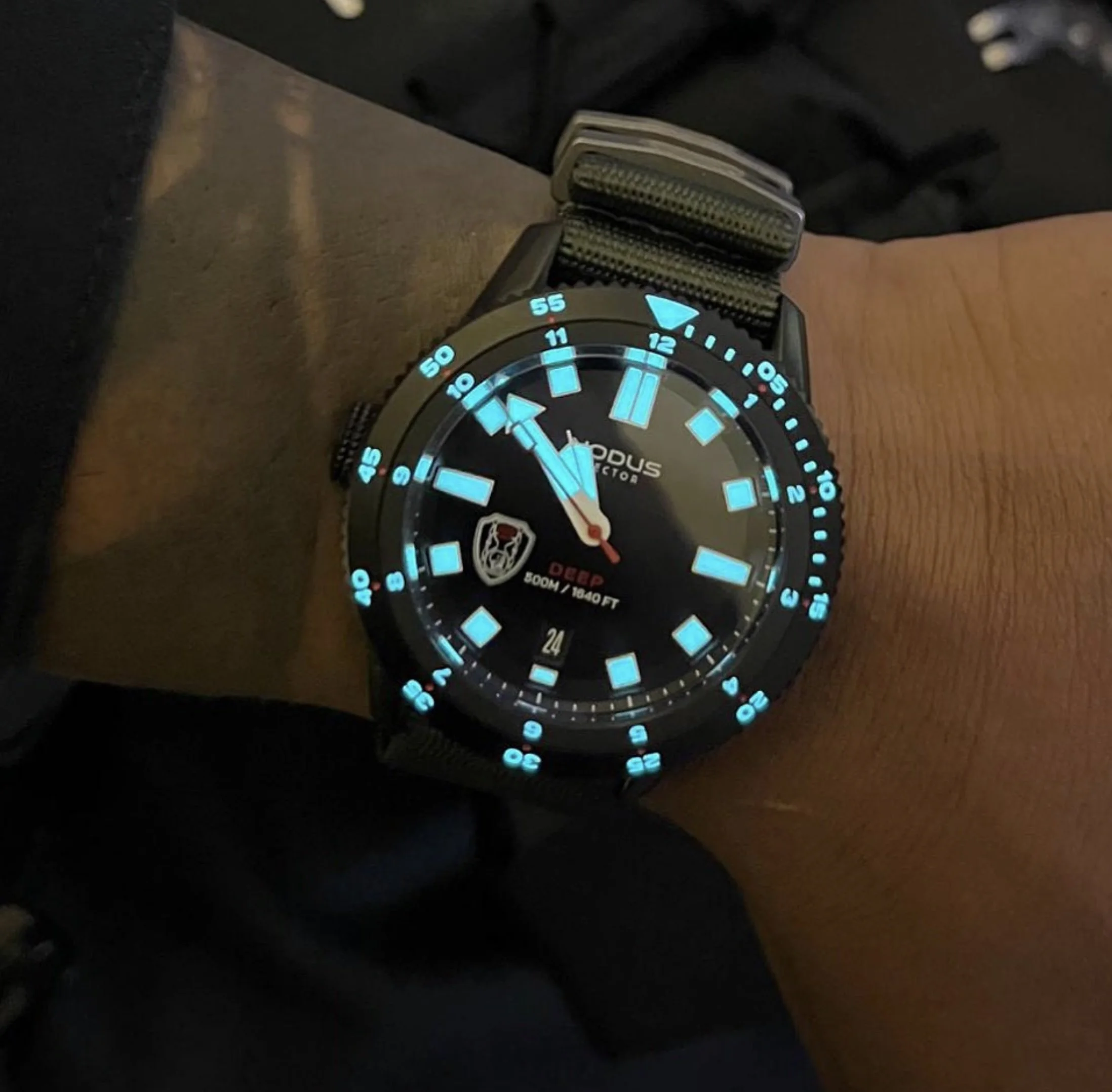 Close-up of a diver's watch face with illuminated blue markers and hands on a wooden surface.