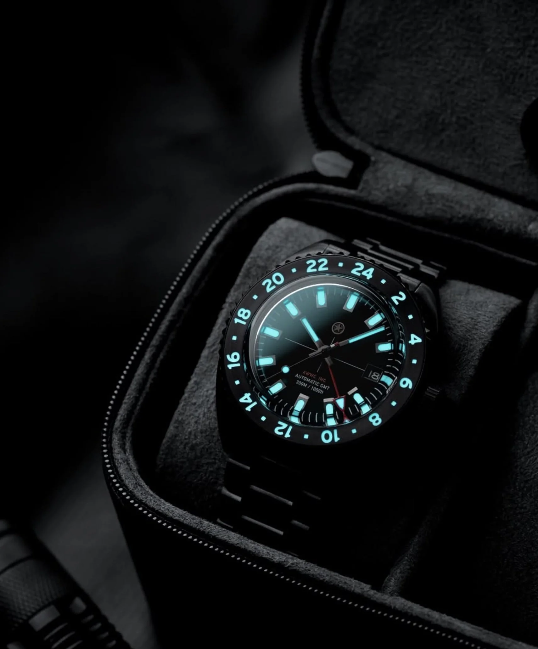 Close-up of a wristwatch with a black strap and a glowing blue dial, nestled in a dark watch box with a textured interior.
