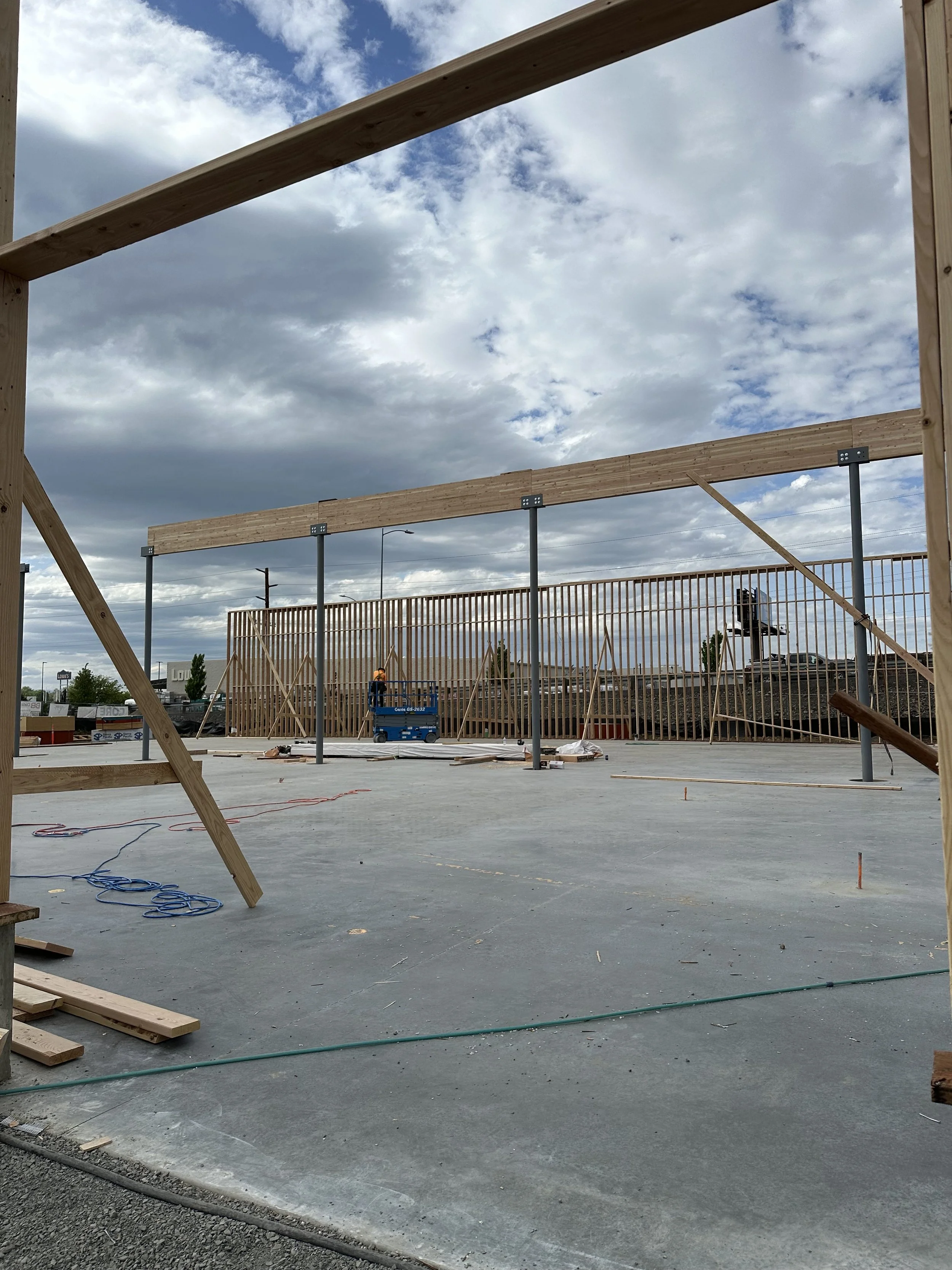 Construction site with wooden framework and metal support beams on a concrete foundation, under partly cloudy sky.