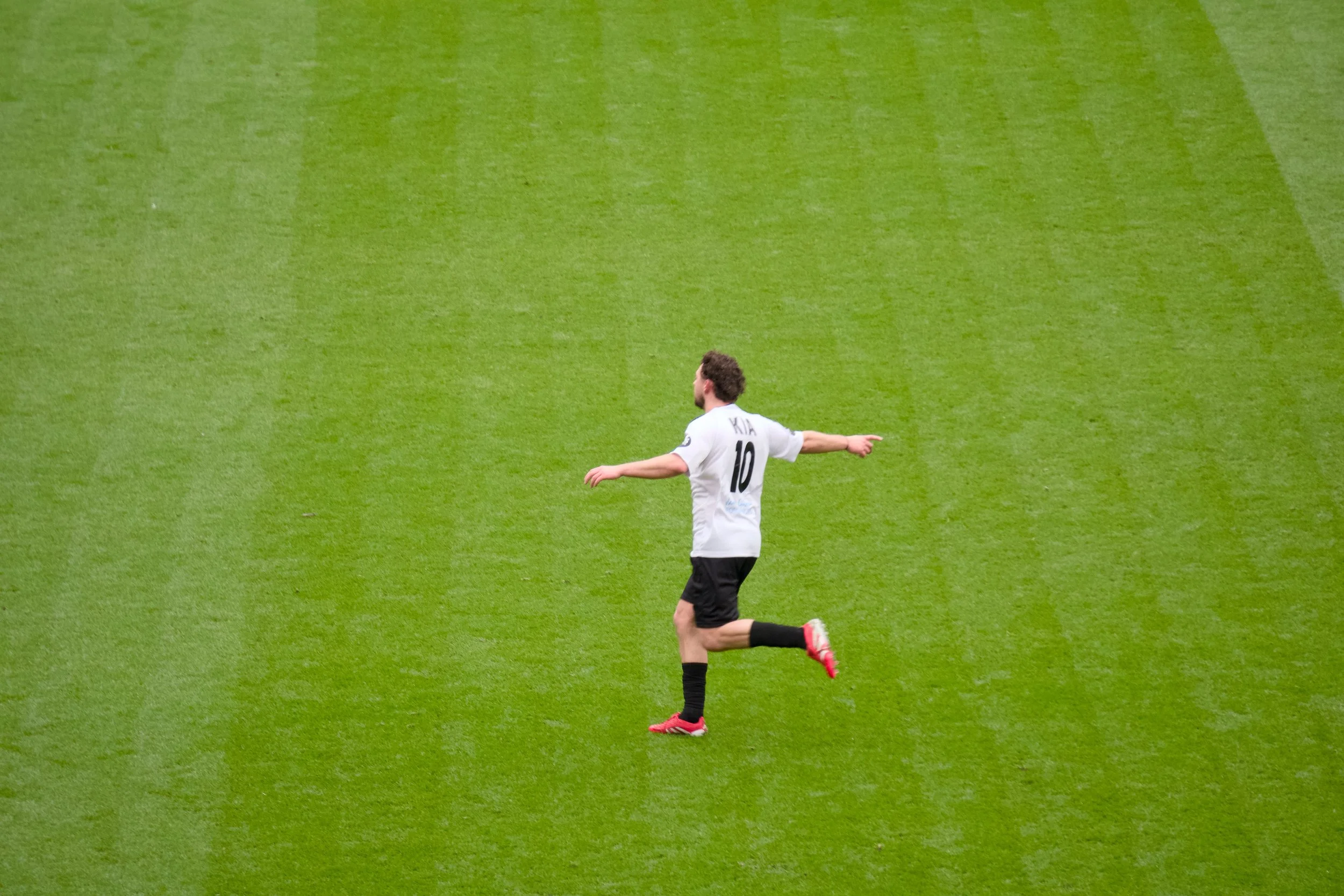 A soccer player wearing a white jersey with the number 10 and the name 'KIA' on the back is running on a green soccer field.