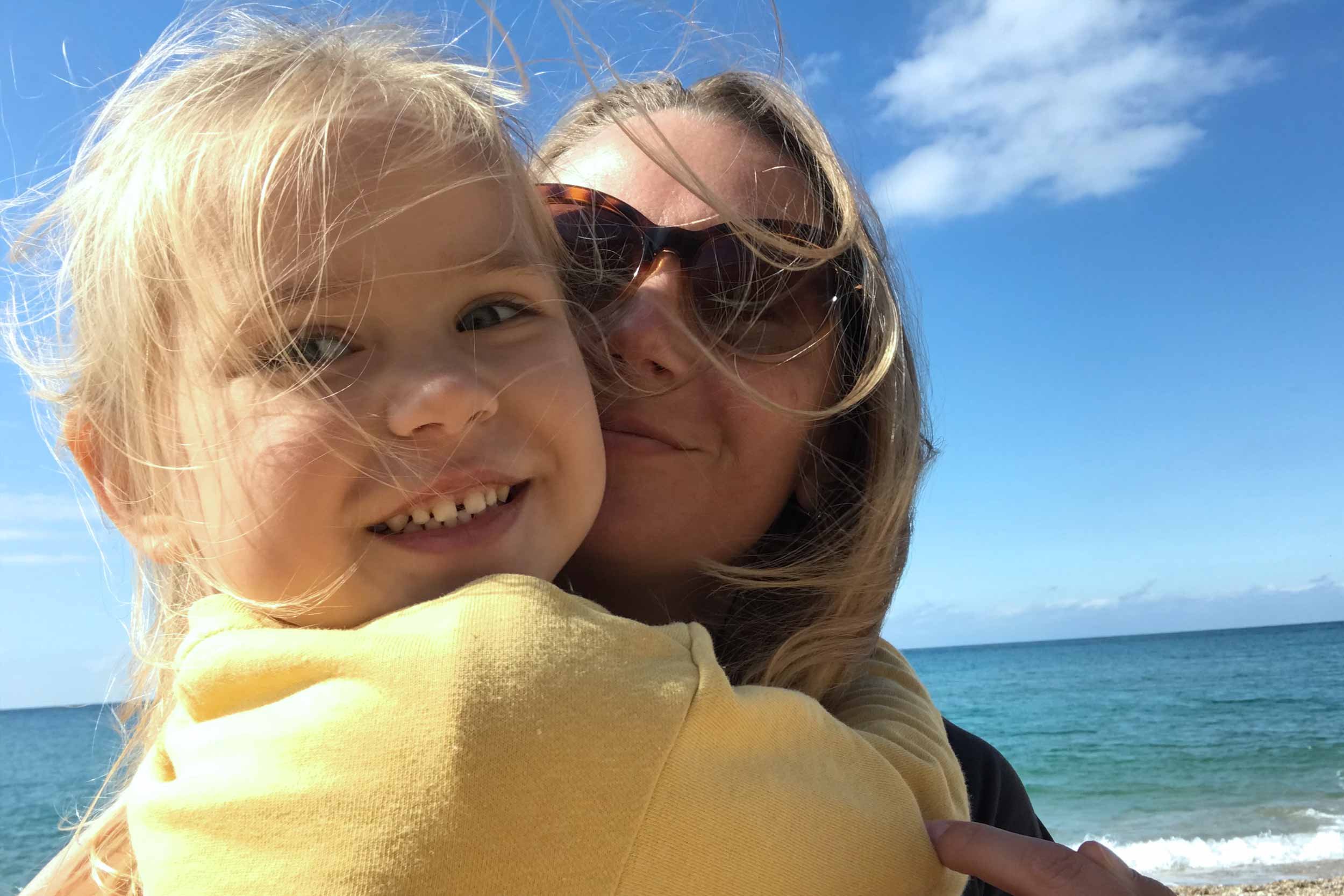 woman with sun glasses hugging young child on the beach