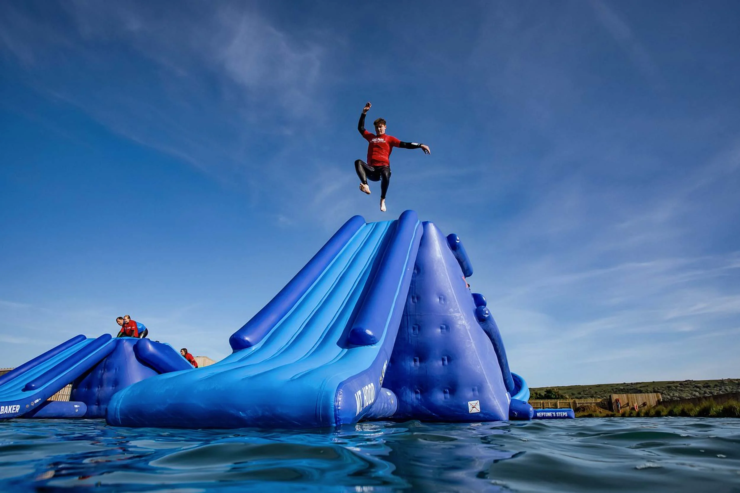 Inflatable water slide with children sliding and playing under a clear blue sky.
