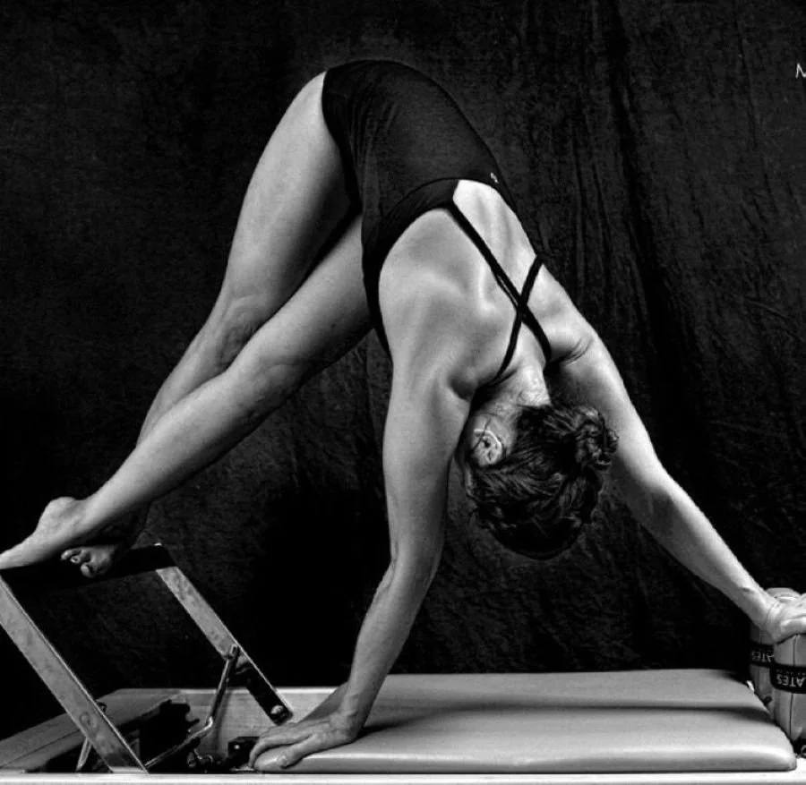 Femme faisant une posture de yoga en position de chien tête en bas, en utilisant une table pour soutenir une jambe, en noir et blanc.