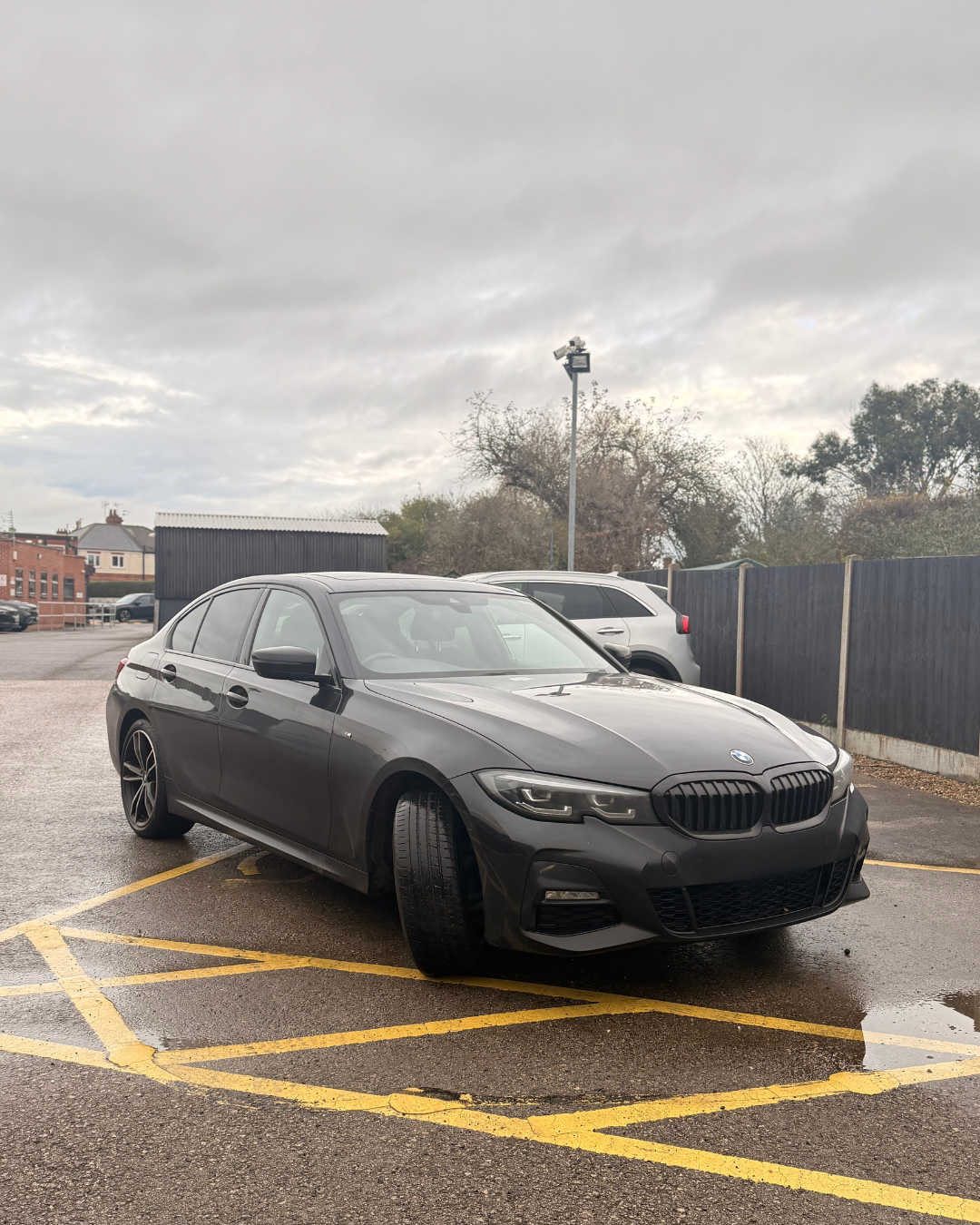 A dark gray BMW parked diagonally in a parking lot on a cloudy day.