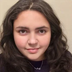 Close-up of a young girl with long dark hair and light skin, looking directly at the camera with a slight smile.