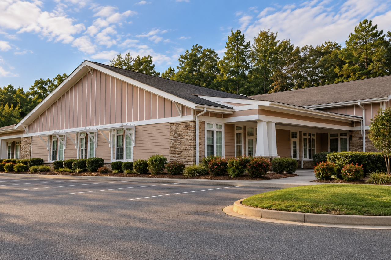 An apartment complex with a parking lot and landscaped bushes, trees, and grass in front.