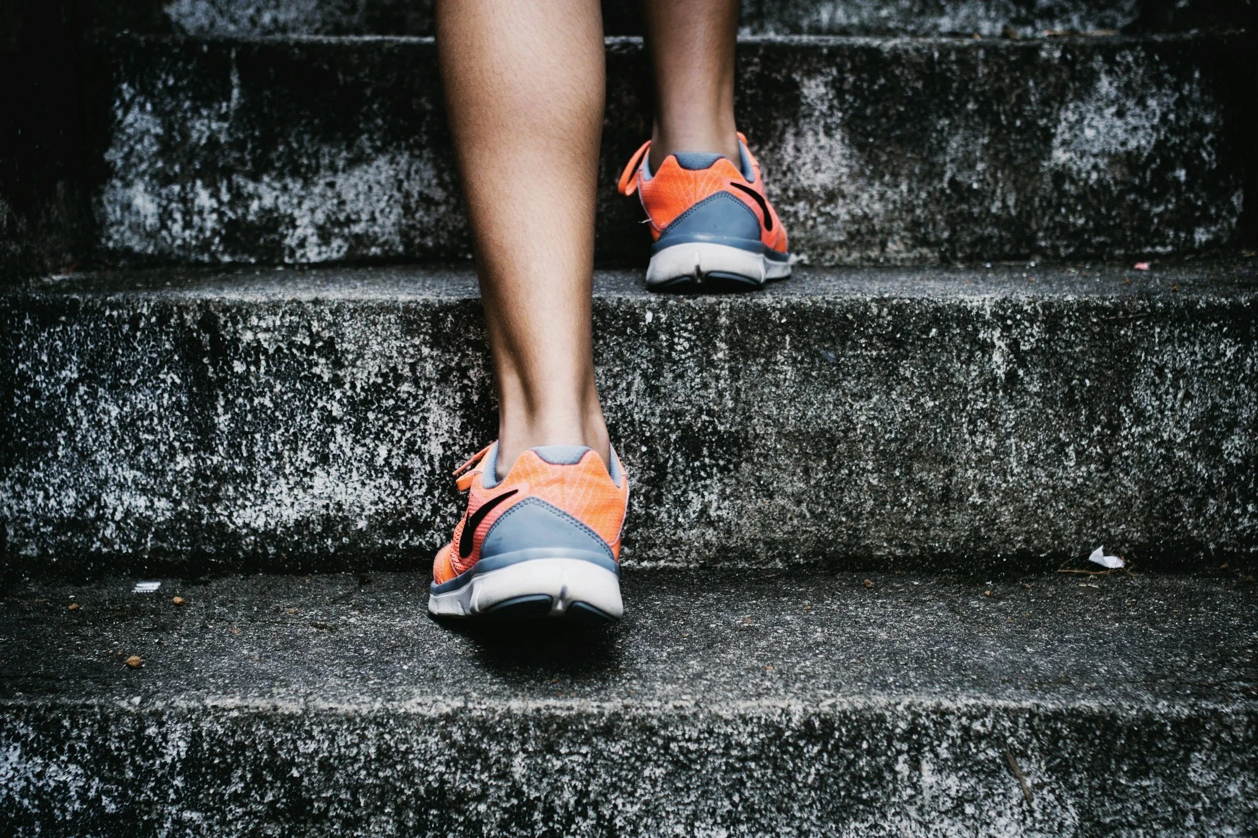 Person climbing outdoor concrete stairs wearing orange and gray athletic shoes.