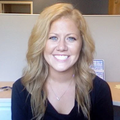 A woman with blonde hair smiling at the camera in an office setting.