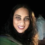 A woman smiling with dark hair and makeup, taking a selfie.