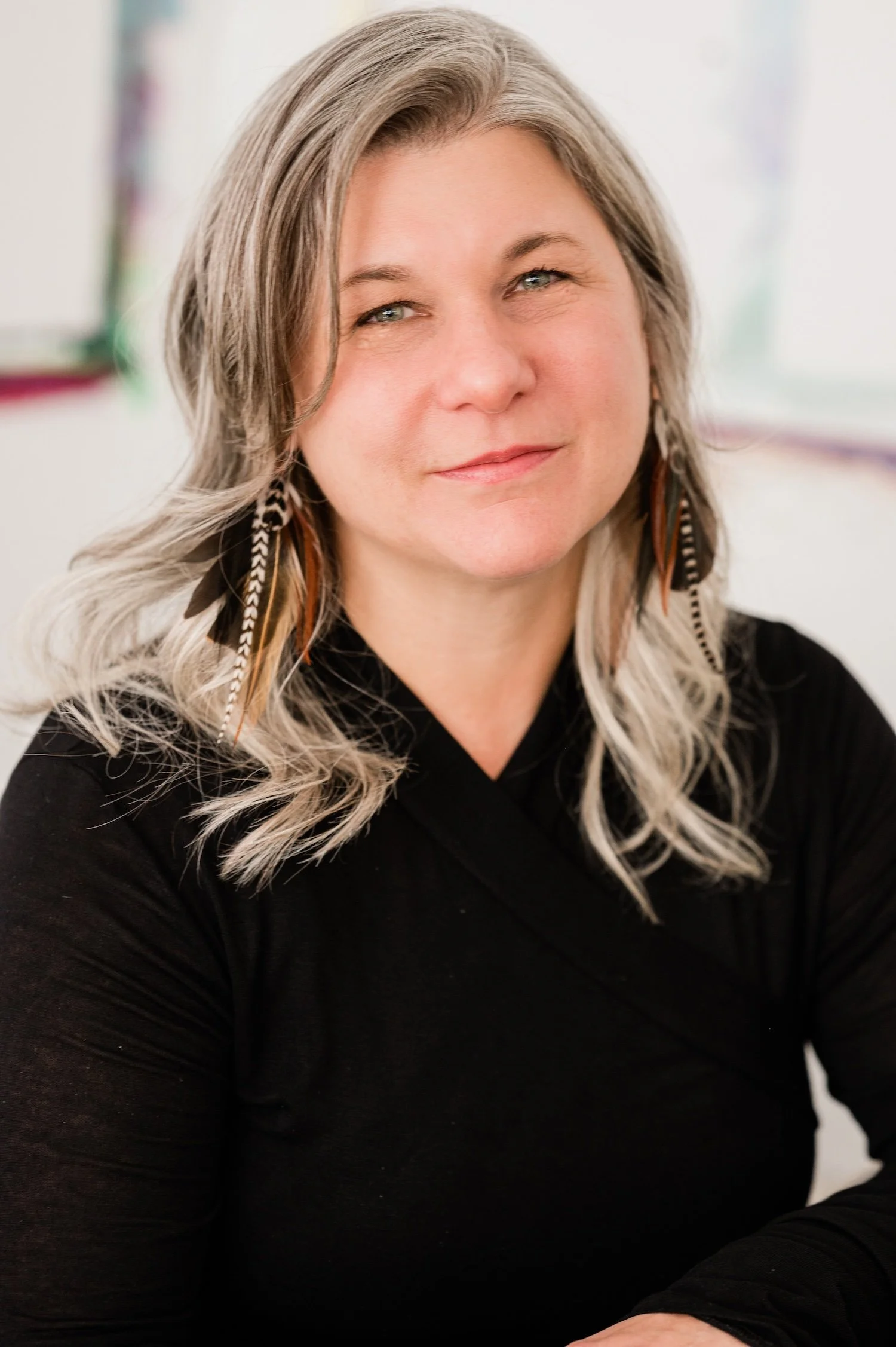 Therapist Dana Keeton smiling with long, wavy gray hair, wearing a black top and feather earrings.
