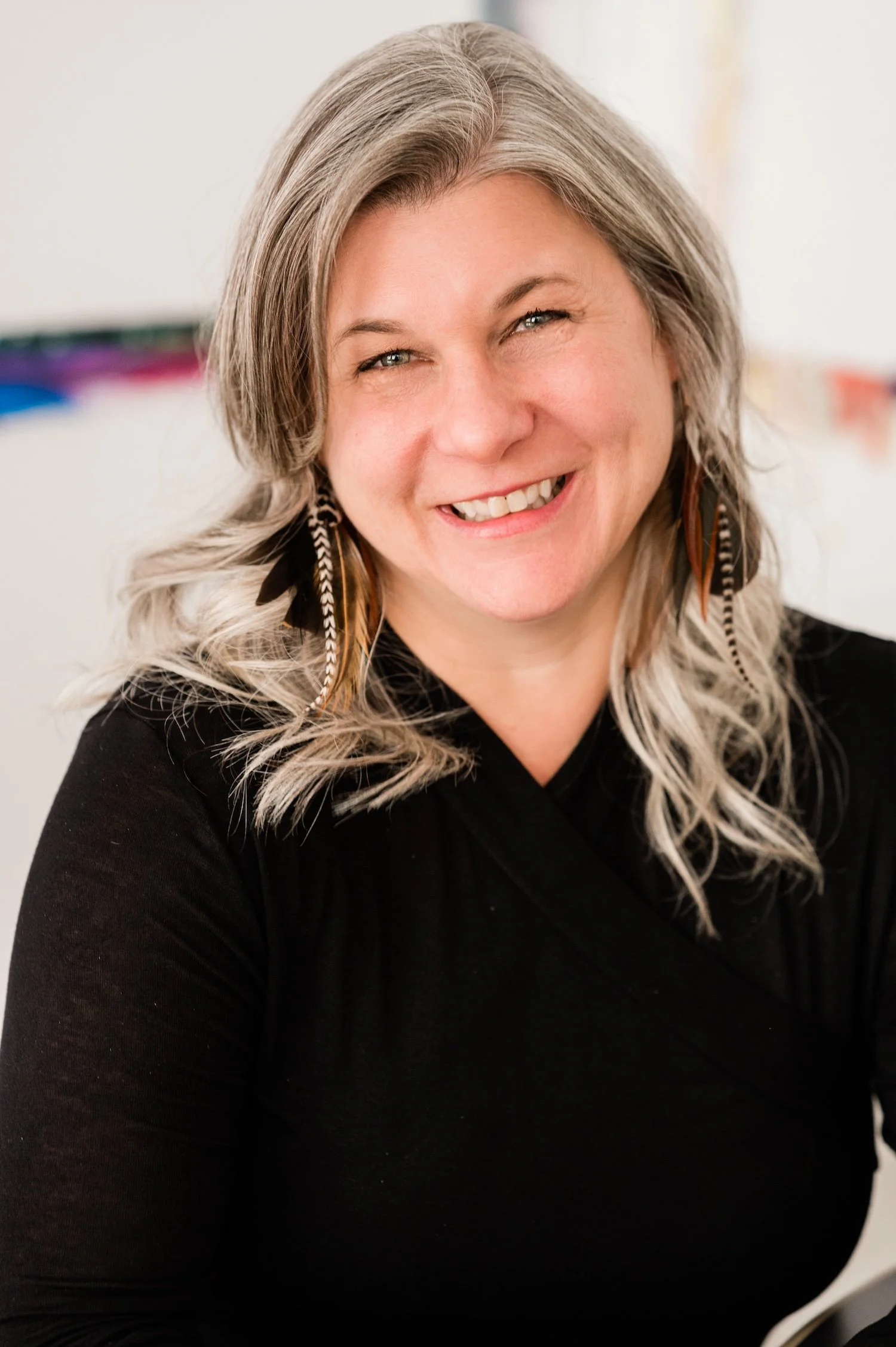 Therapist Dana Keeton smiling with long, wavy gray hair, wearing a black top and feather earrings.