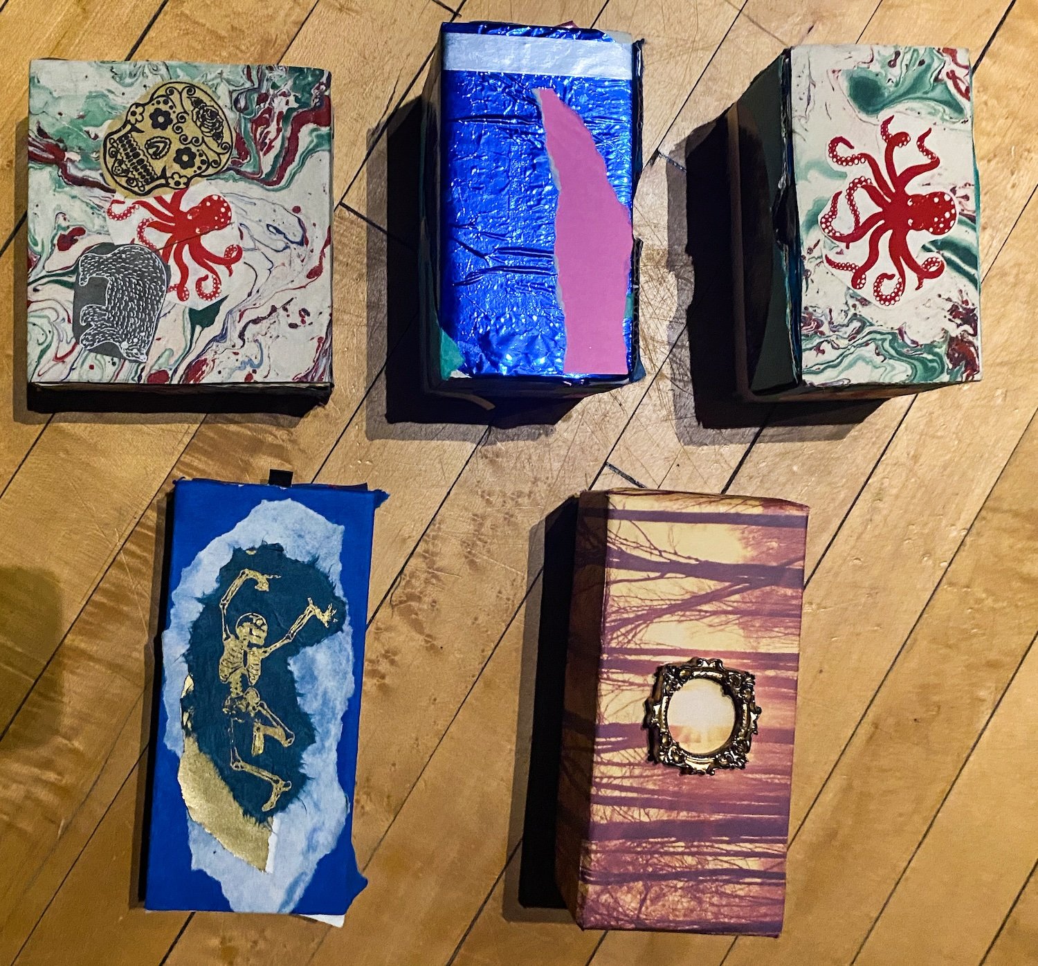 Five decorated boxes with various artistic designs on a wooden floor.