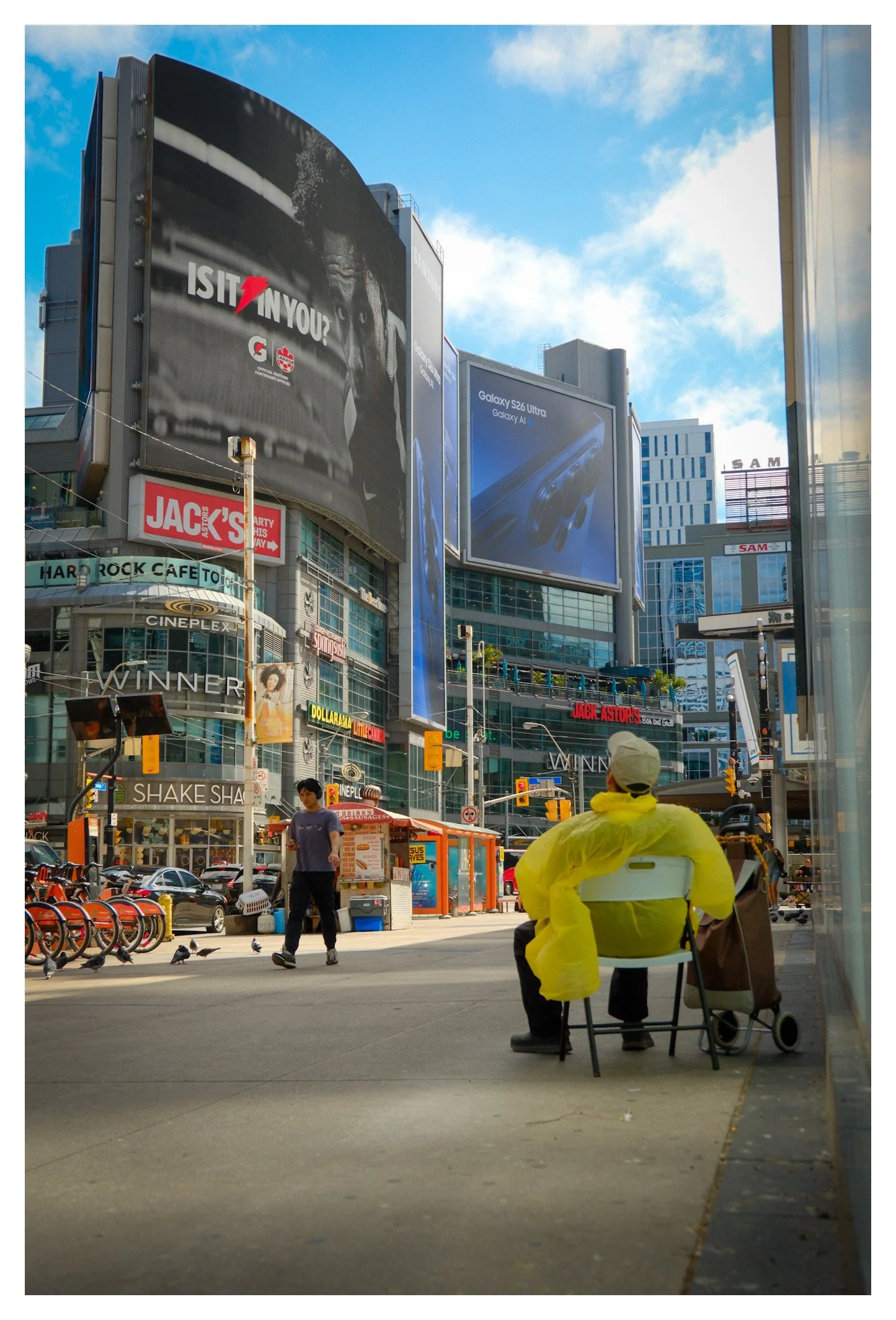 Bright screens, busy streets, and a single quiet figure create a striking contrast in the heart of downtown Toronto. A candid moment that captures the city's unique character.