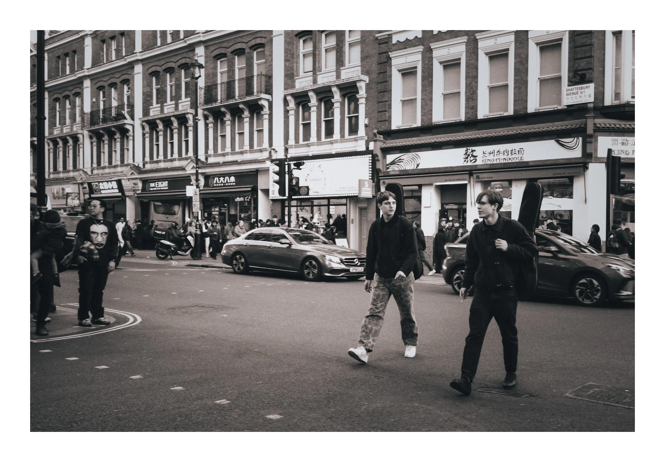 Two men with a guitar slung over their backs, crossing a London street—capturing a quiet moment of rhythm, movement, and urban storytelling.
