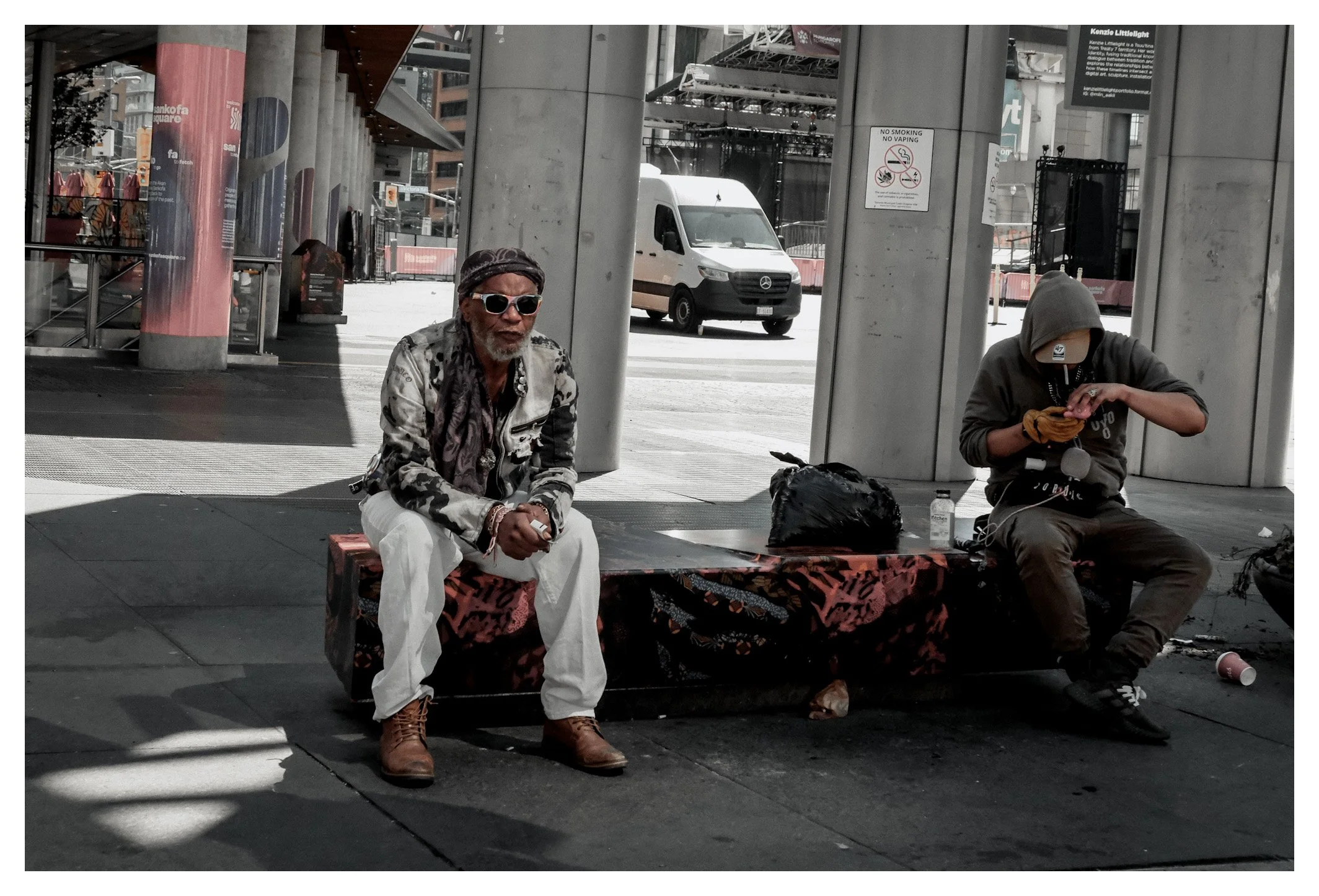 A city is a place where countless lives unfold side by side. This frame captures two individuals sharing the same space, each immersed in a completely different story.