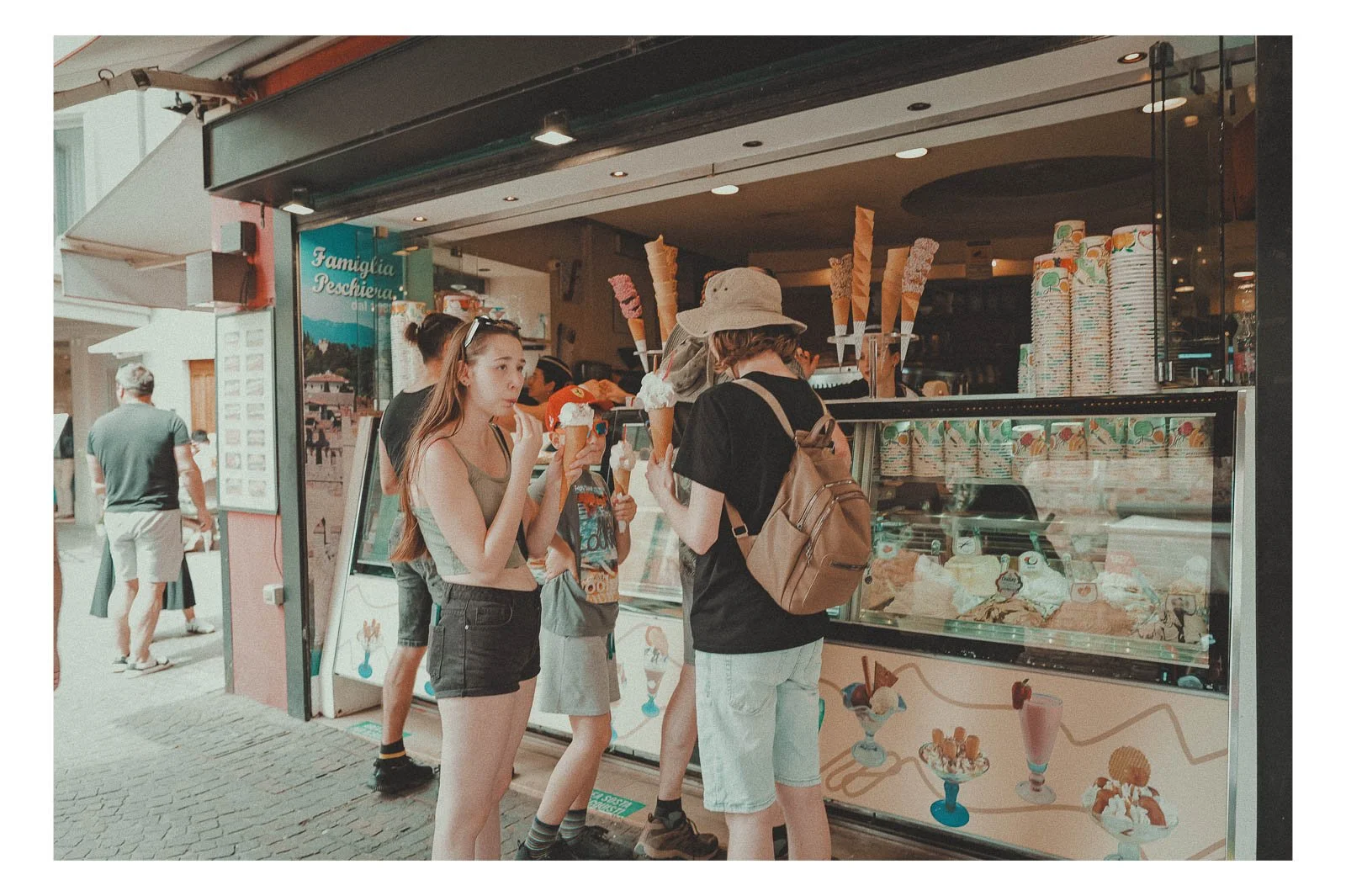 People gather in front of an ice cream shop on a warm summer day.
Laughter, movement, and melting scoops fill the air with a sense of ease and joy.
It’s a simple scene that captures the rhythm of summer and everyday life.