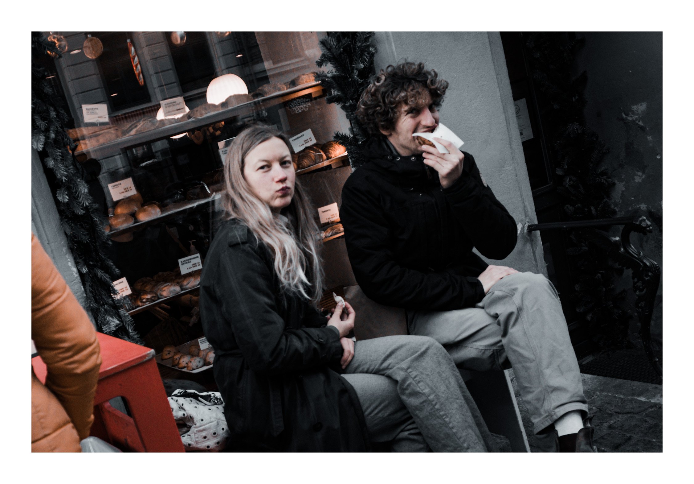 Two people sit outside together, talking and laughing, while one of them bites into a simple cheese roll. The moment is quiet and everyday — but somehow warm and real. It feels like the kind of small memory you keep with you.