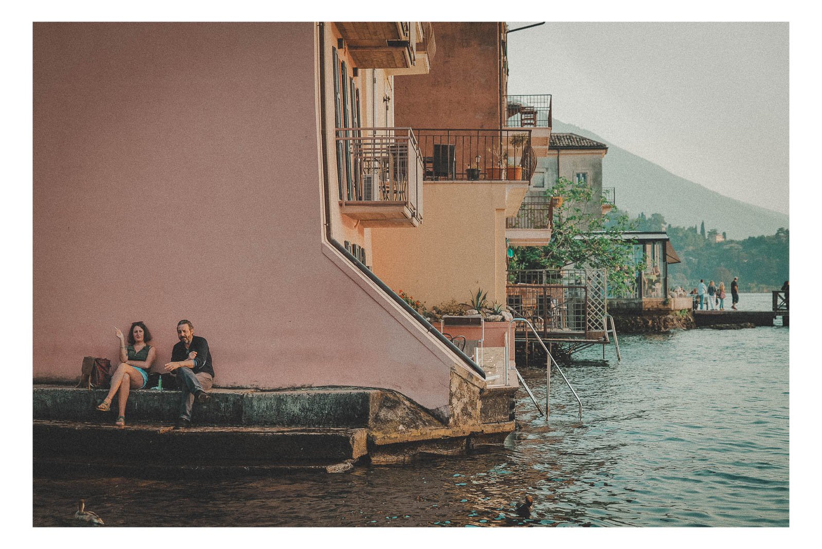 A couple sitting at the edge of a house, overlooking Lake Garda, shares a quiet, unspoken moment.
The view opens toward the water, framed by light, distance, and stillness.
It’s a scene where intimacy and landscape blend into one peaceful image.