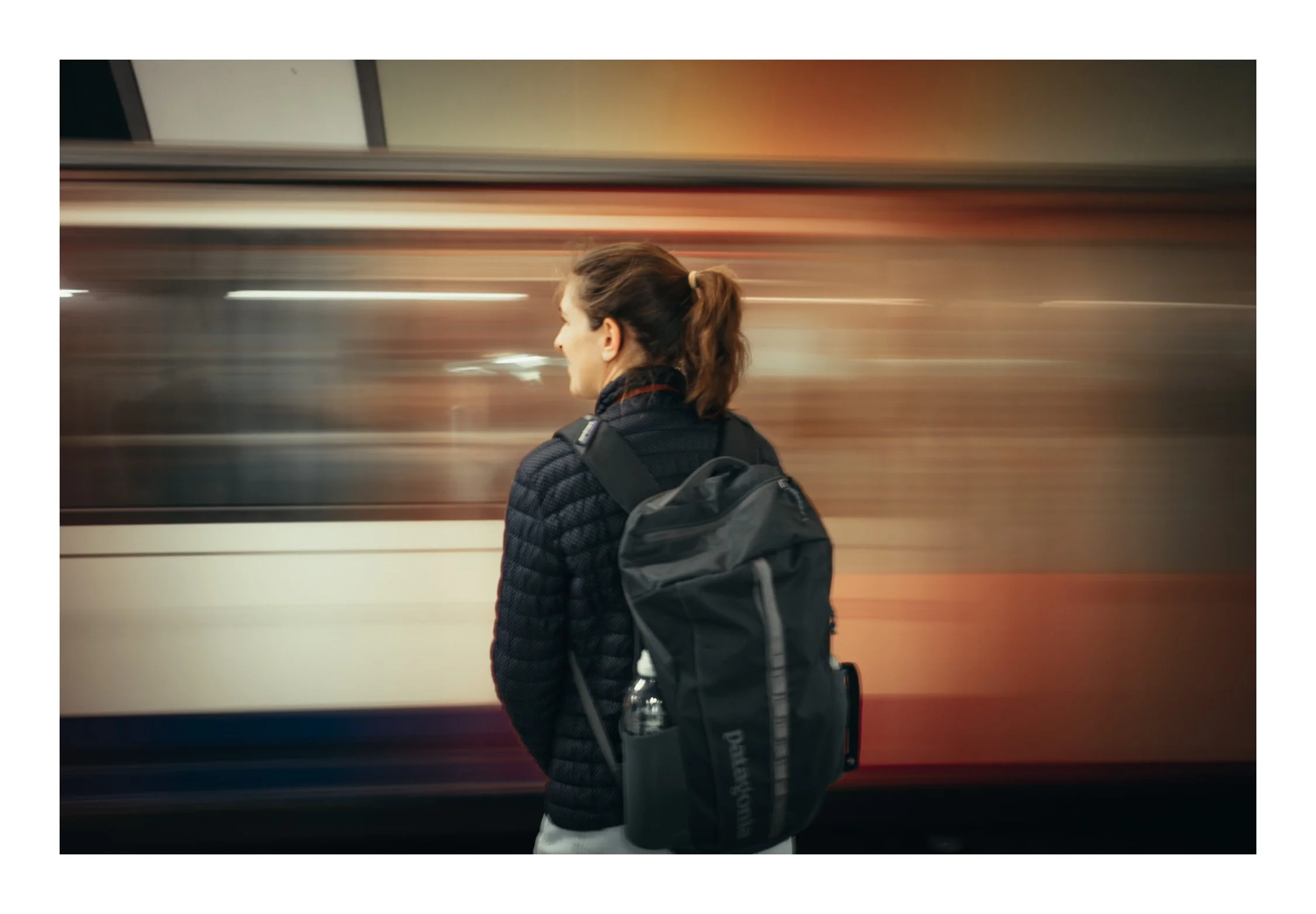 A metro train pulling in as a woman waits—capturing a quiet moment of anticipation within the rhythm of the city.