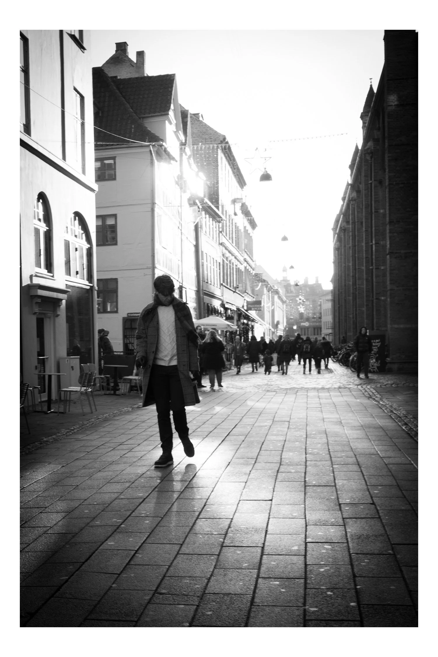 A man walks down the shopping street, empty-handed, just taking everything in. He isn’t carrying any bags — he’s simply wandering, watching the lights, the shops, and the people around him. It feels calm and unhurried, like he has all the time in the