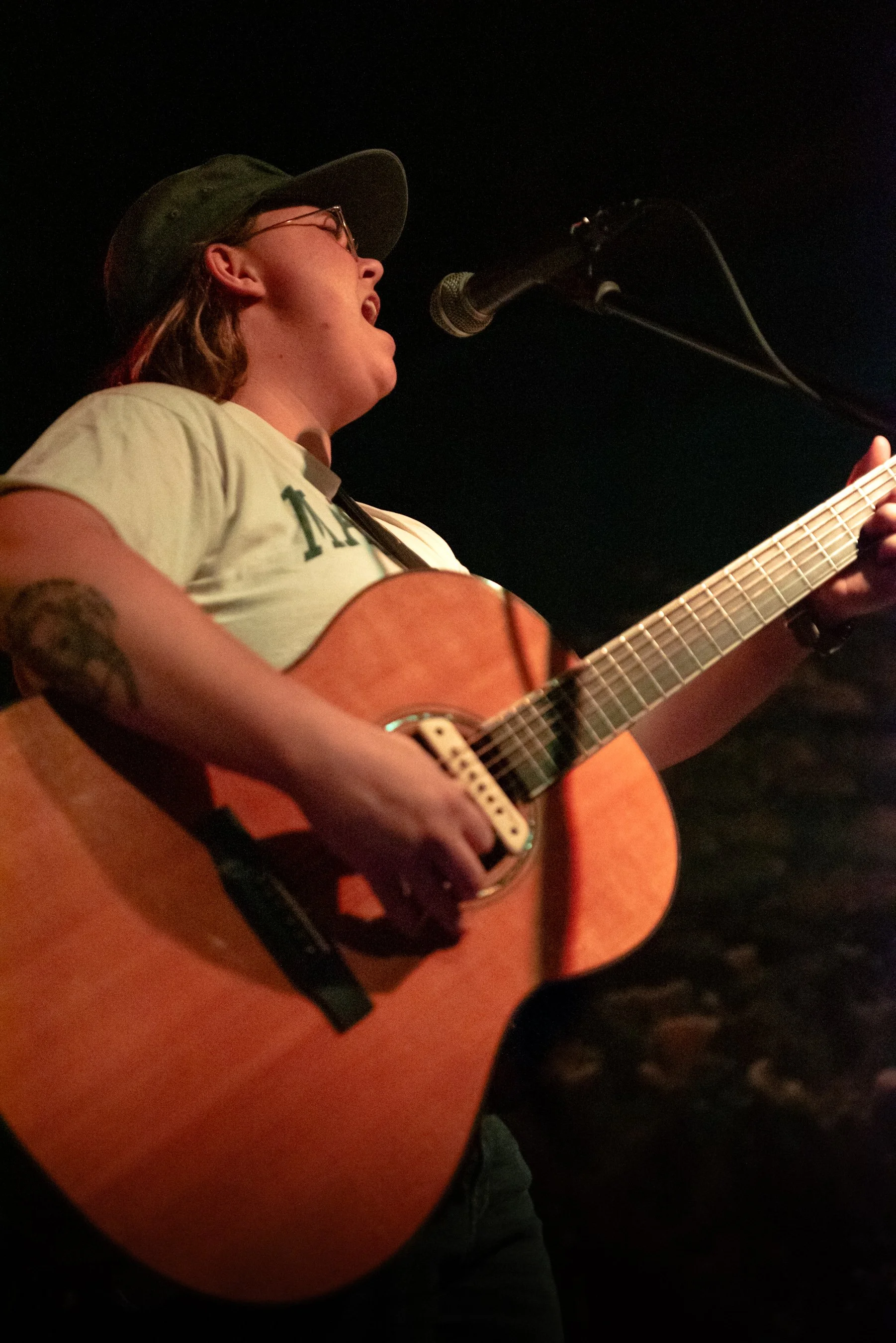 Person singing into a microphone while playing an acoustic guitar on stage.