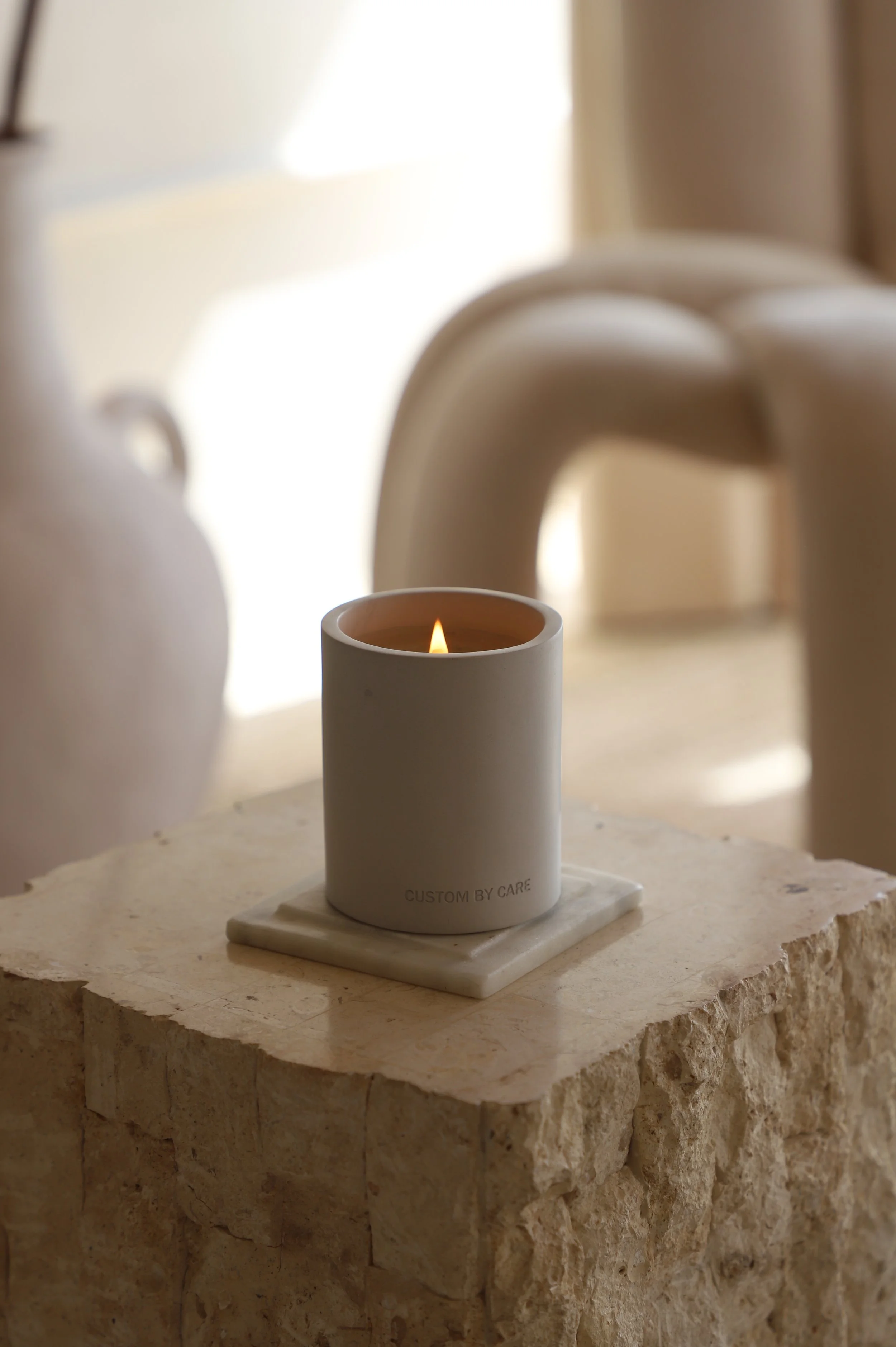 A lit white candle on a stone surface in a softly lit room.
