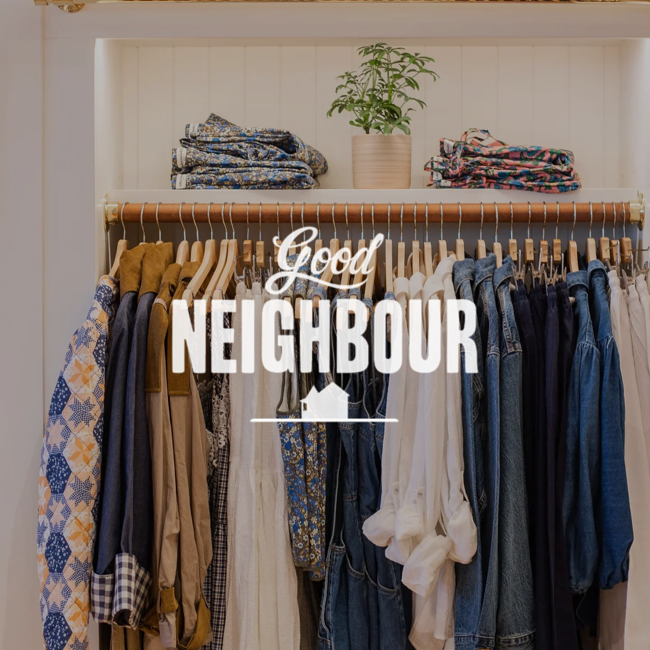 Clothing rack with various shirts, pants, and jackets, above is a shelf with folded clothes and a potted plant, with the words 'Good Neighbour' overlayed.