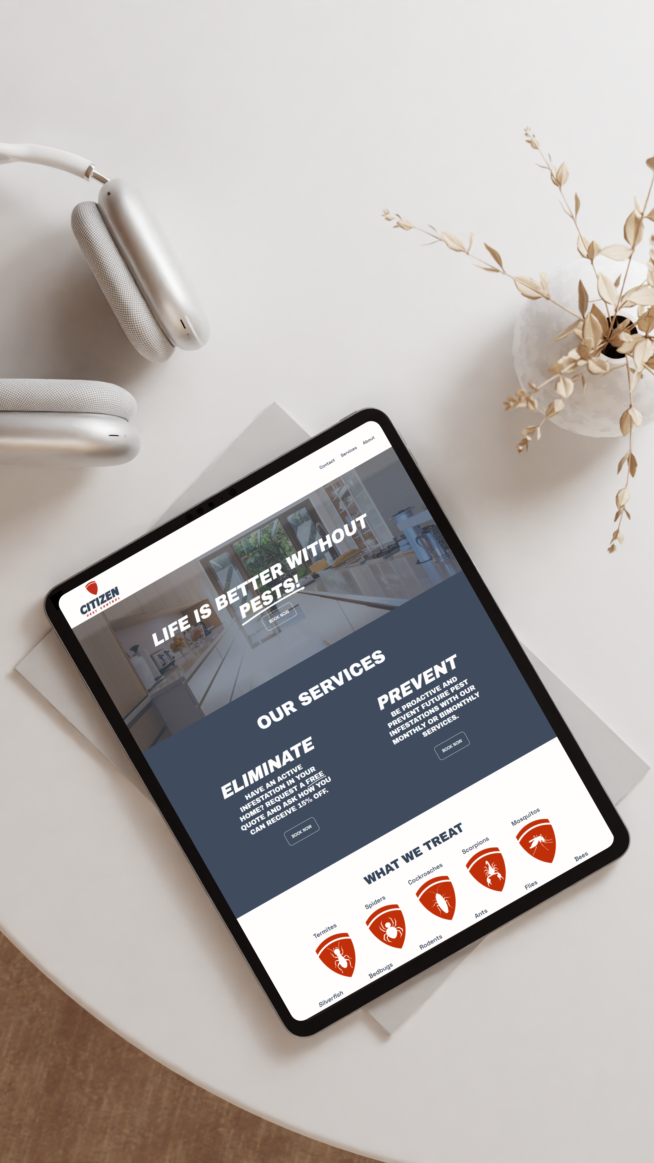 Tablet on a white table displaying a pest control service website, with a white headphone and a white vase with dried leaves nearby.