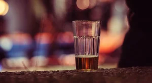 A half-finished beer on a bar, with warm ambient lighting and a silhouette in the background