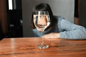 A person sitting at a table looking at a glass of water in a wine glass