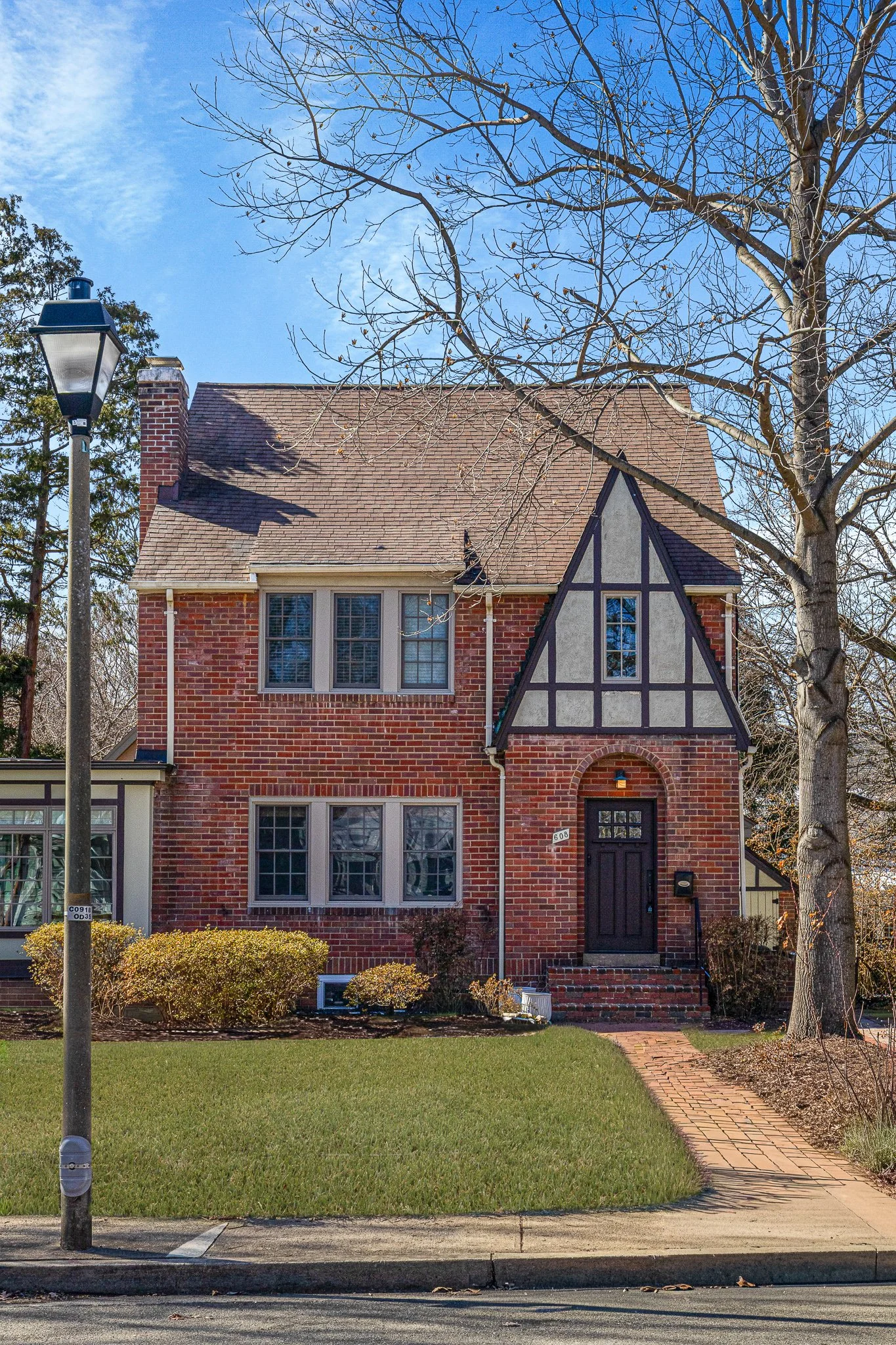 A brick house with black and gray trim, a chimney, and leafless trees in front, under a blue sky.
