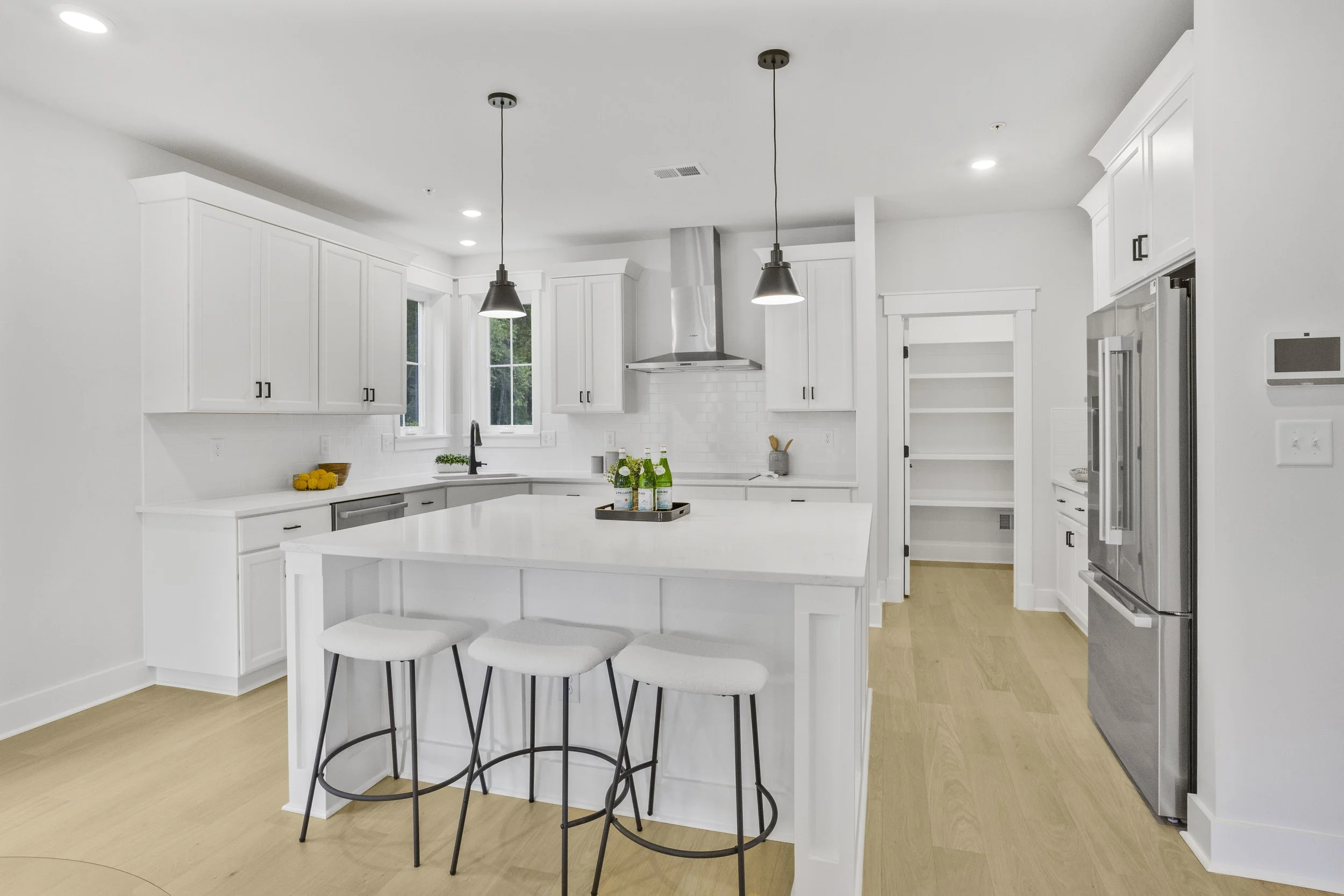 Modern white kitchen with pendant lighting over island, stainless steel appliances, and light wood flooring.