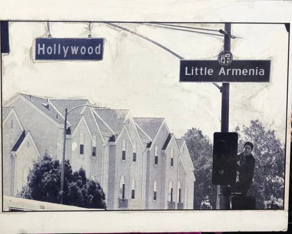 Black and white photo of street signs at an intersection, with one sign reading 'Hollywood' and the other reading 'Little Armenia.'