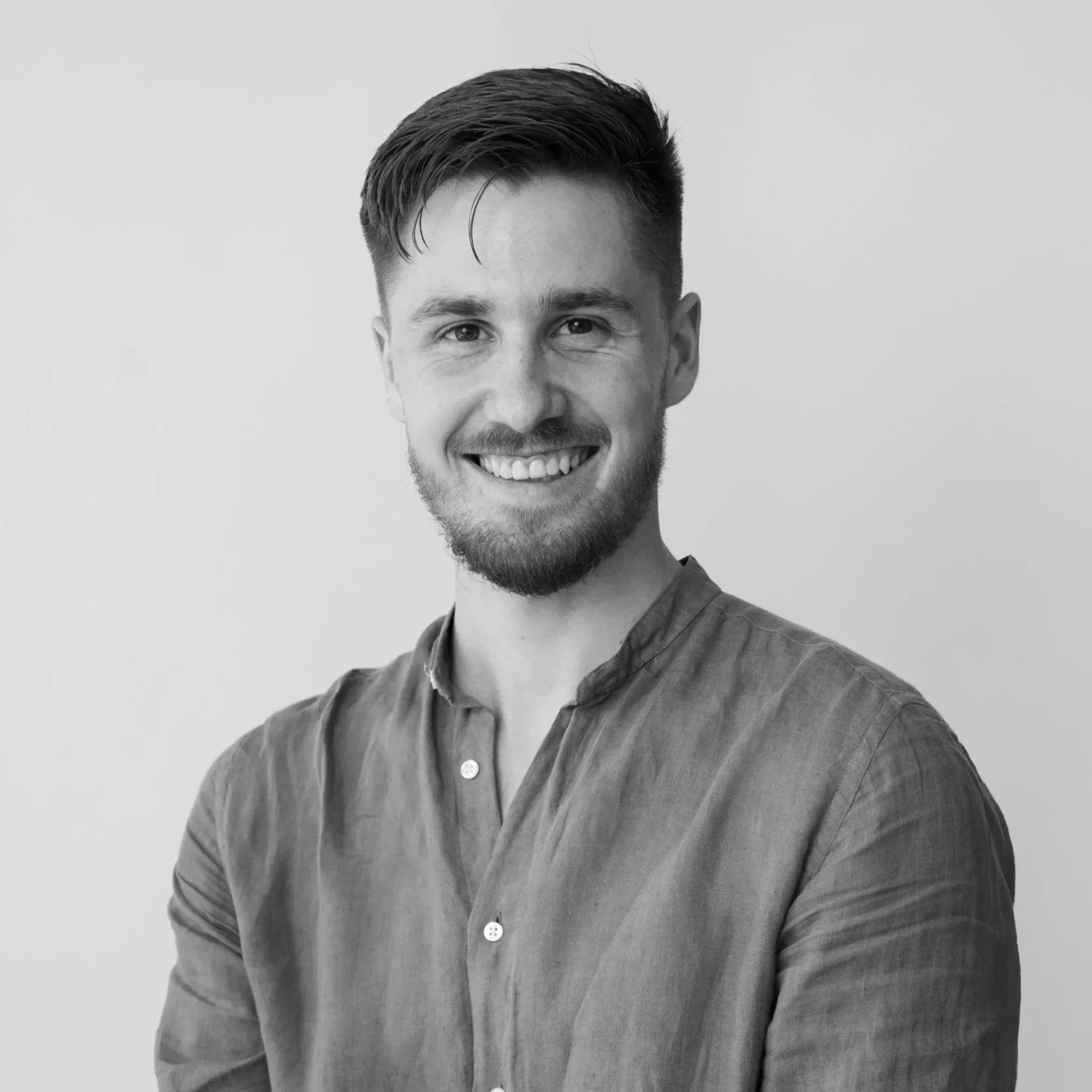 Black and white portrait of a young man smiling, with short wavy hair, beard, and wearing a button-up shirt.