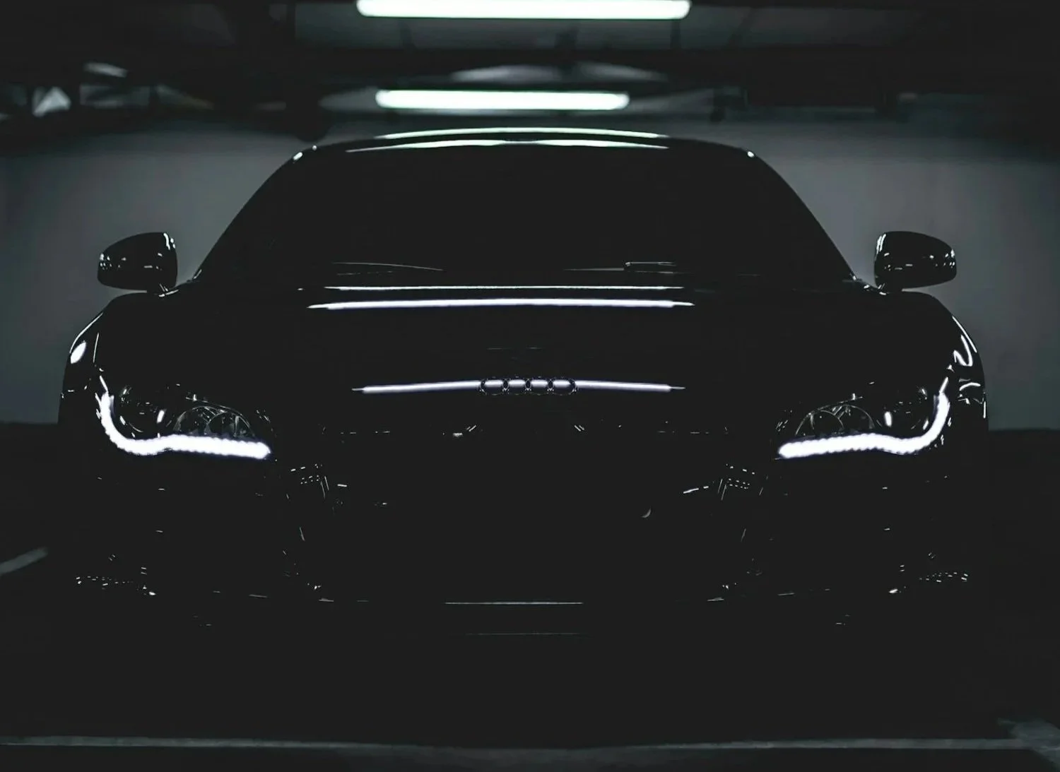A black car with illuminated headlights parked in a dimly lit underground garage.