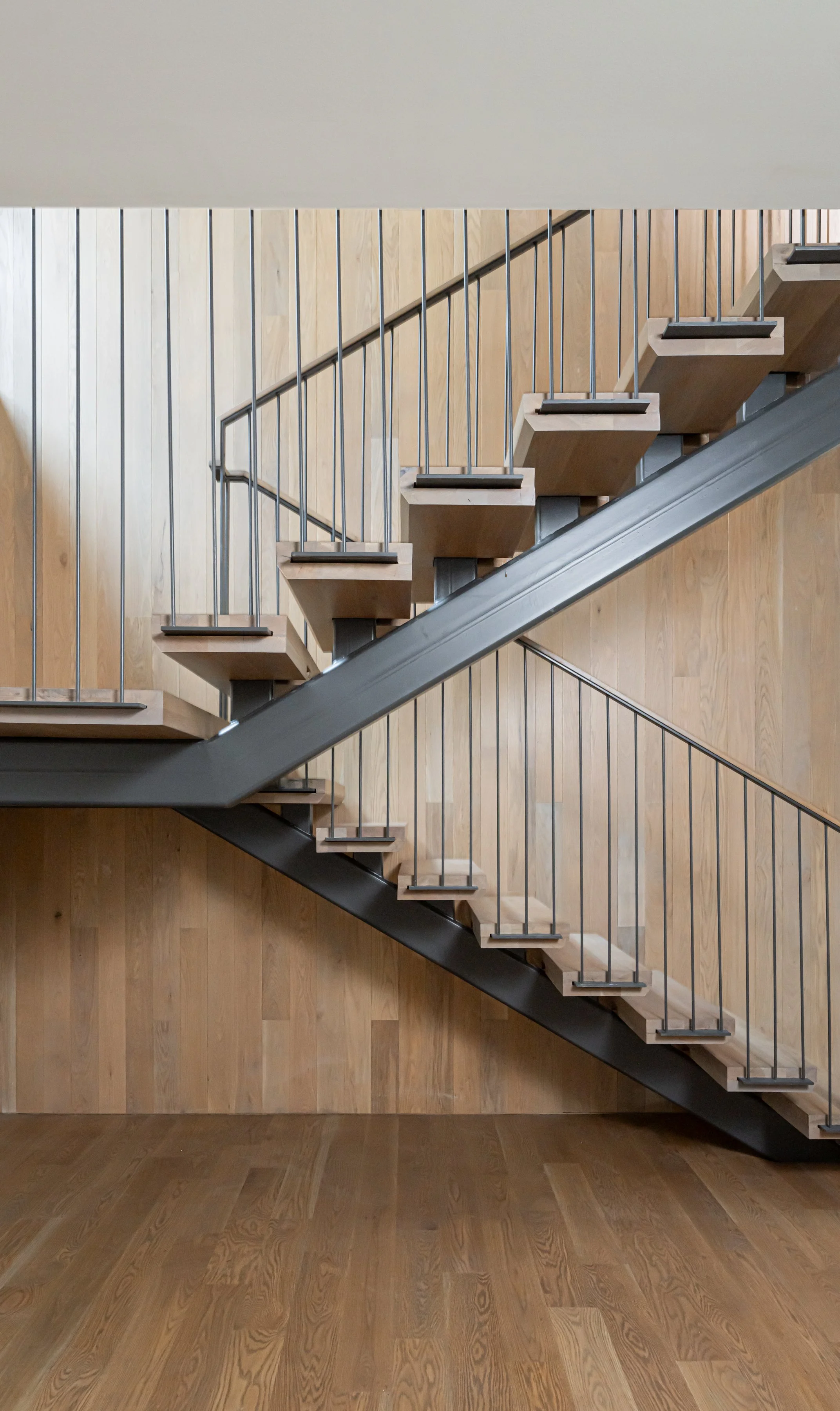 Modern wooden staircase with metal railings and paneling on the wall.