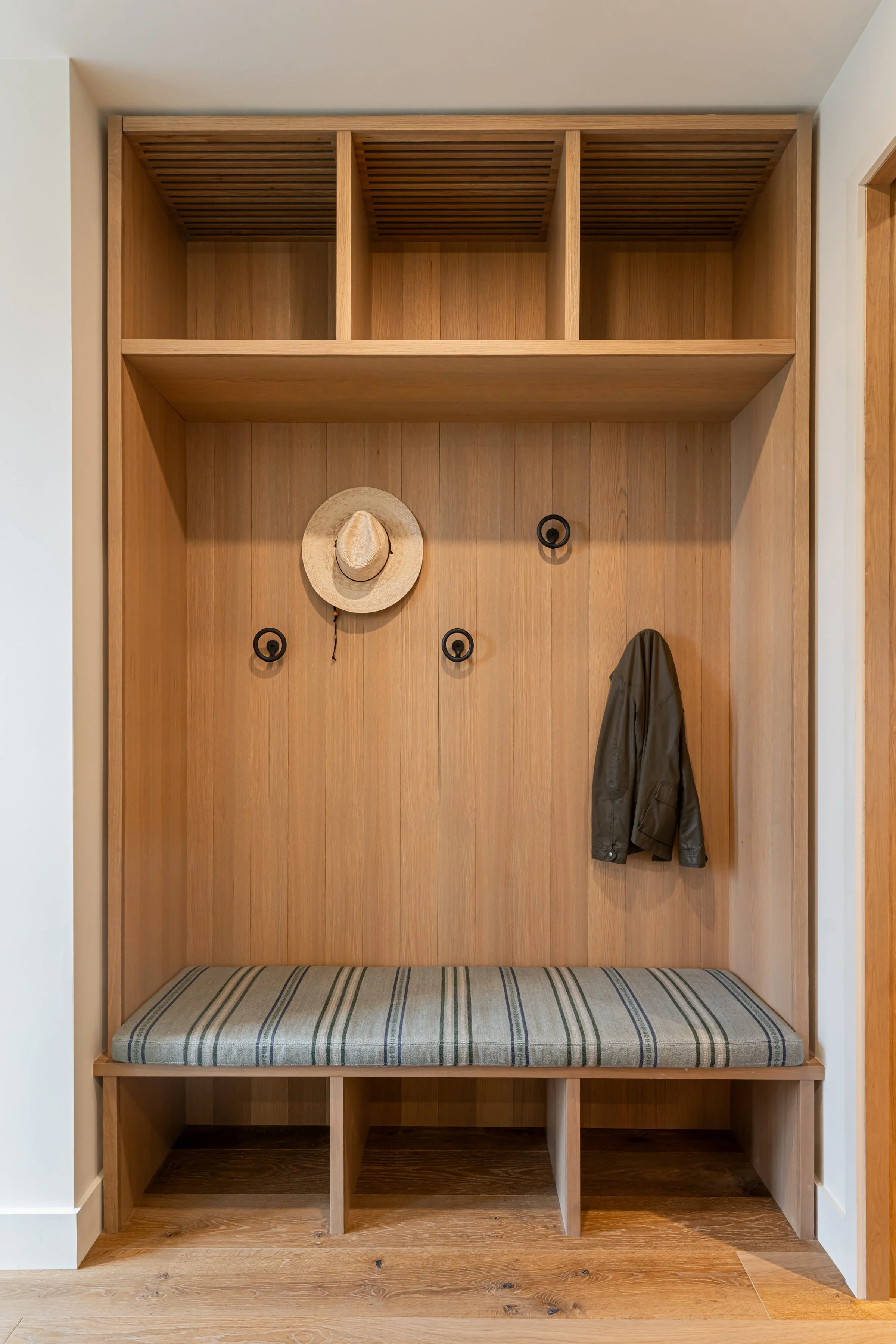 Wooden hallway with hooks holding a hat and a jacket, cushioned bench, open shelves, and hooks.