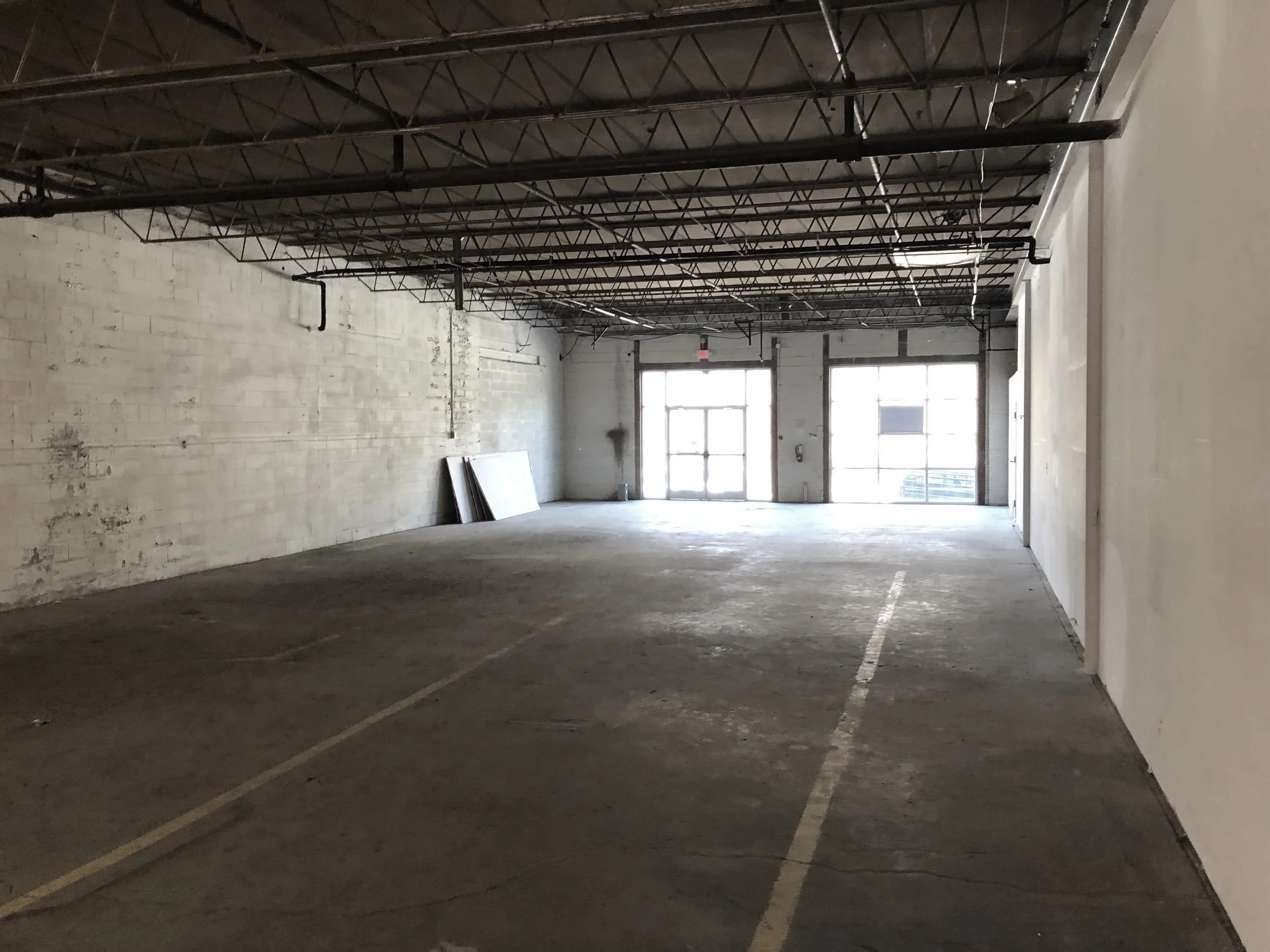 Empty indoor parking garage with marked parking spots, concrete walls, and natural light coming through the large front windows.