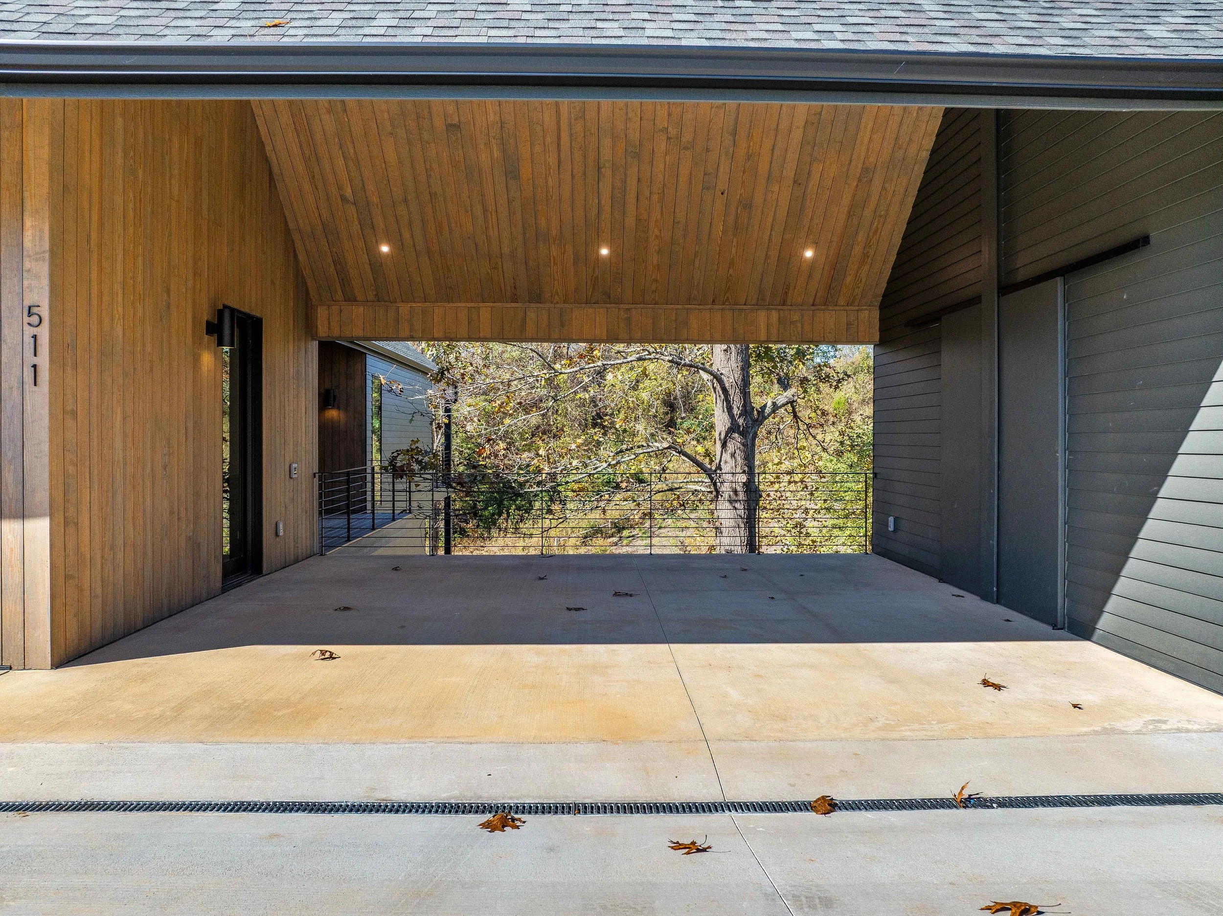 Empty covered carport with wood-paneled ceiling, concrete floor, and a view of trees and neighborhood homes.